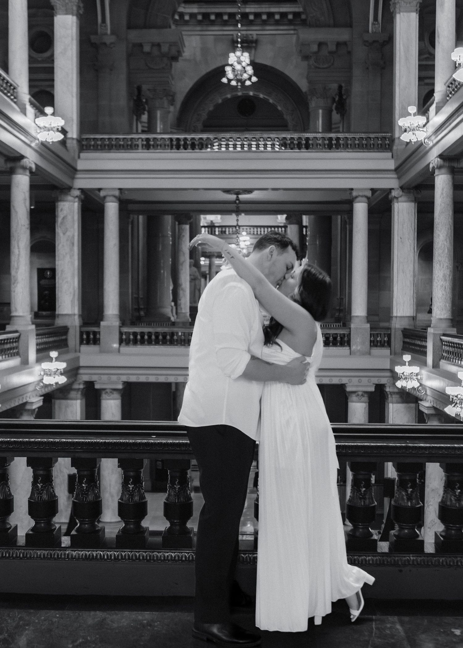 Black and white romantic photo of a couple embracing and kissing inside an ornate building.