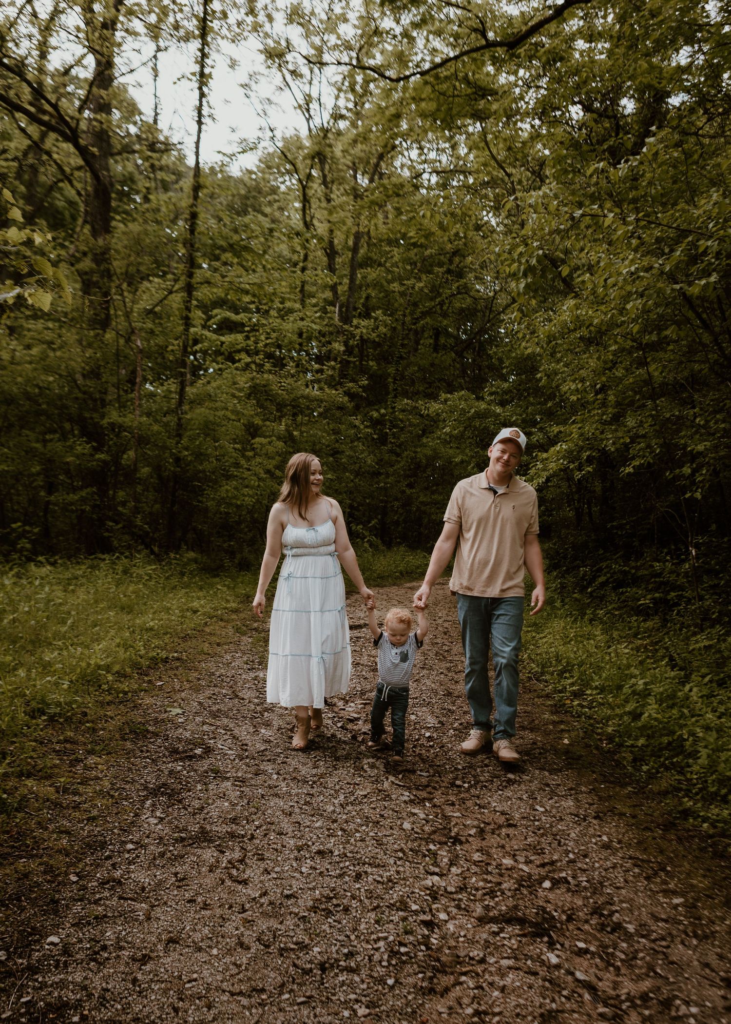 Young family of three walking hand in hand along wooded forest trail together.