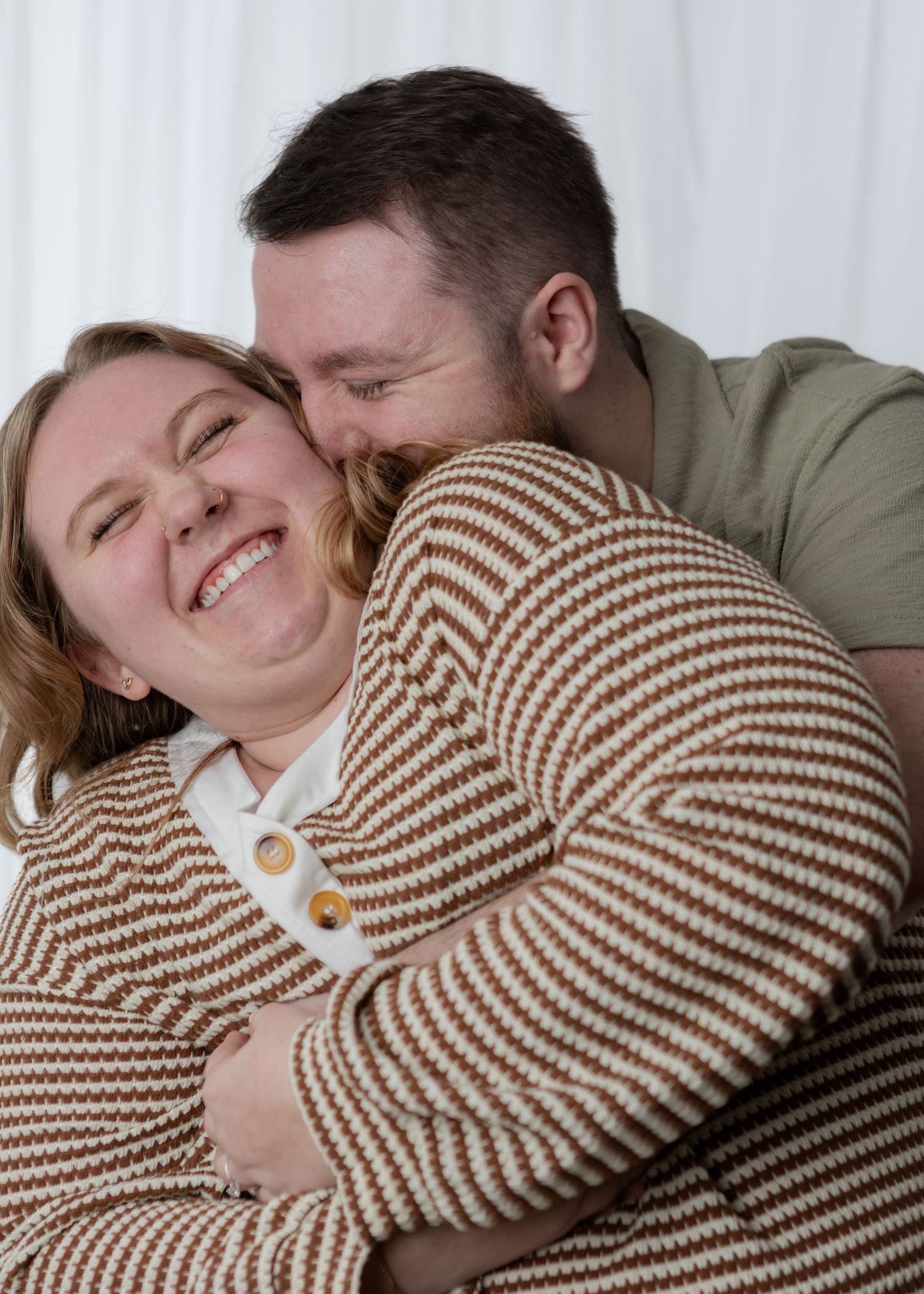 Happy couple embracing and laughing together, wearing matching brown striped sweaters indoors.