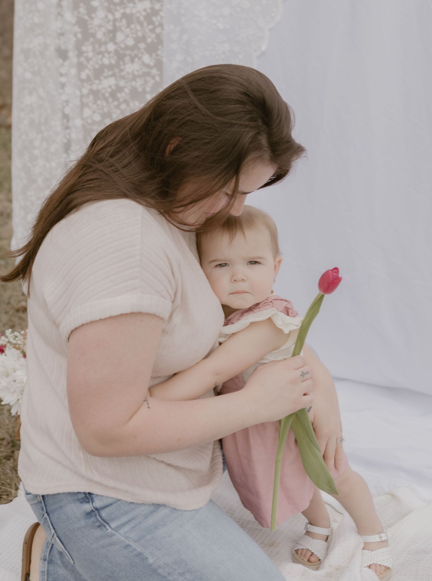 Mother holding baby girl with a red tulip during an outdoor spring photo session.