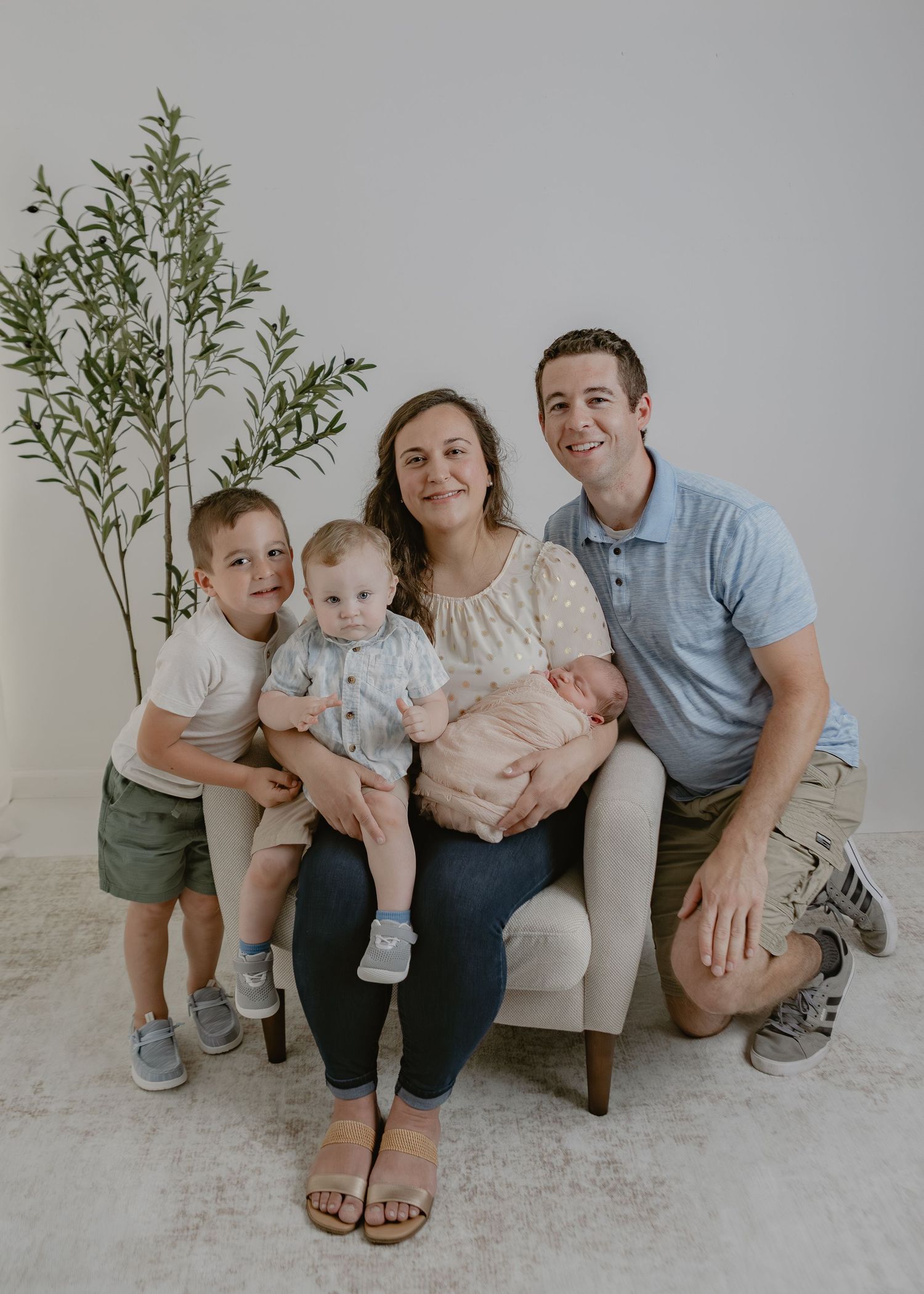 Happy family of five with newborn baby posing for a portrait in a bright studio.