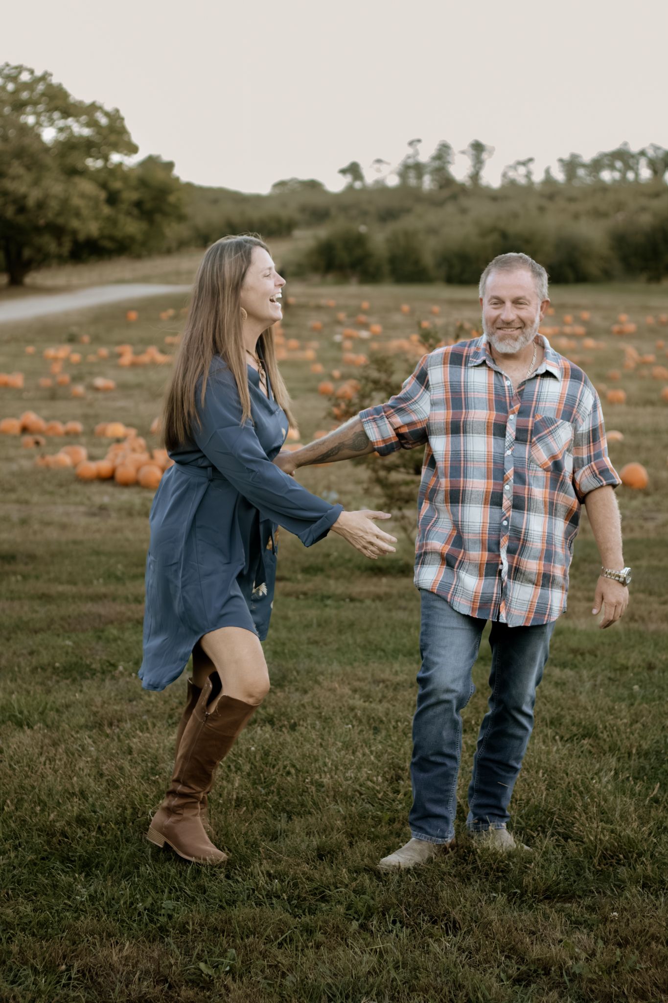 Joyful couple laughing and dancing together in a scenic autumn pumpkin patch field.