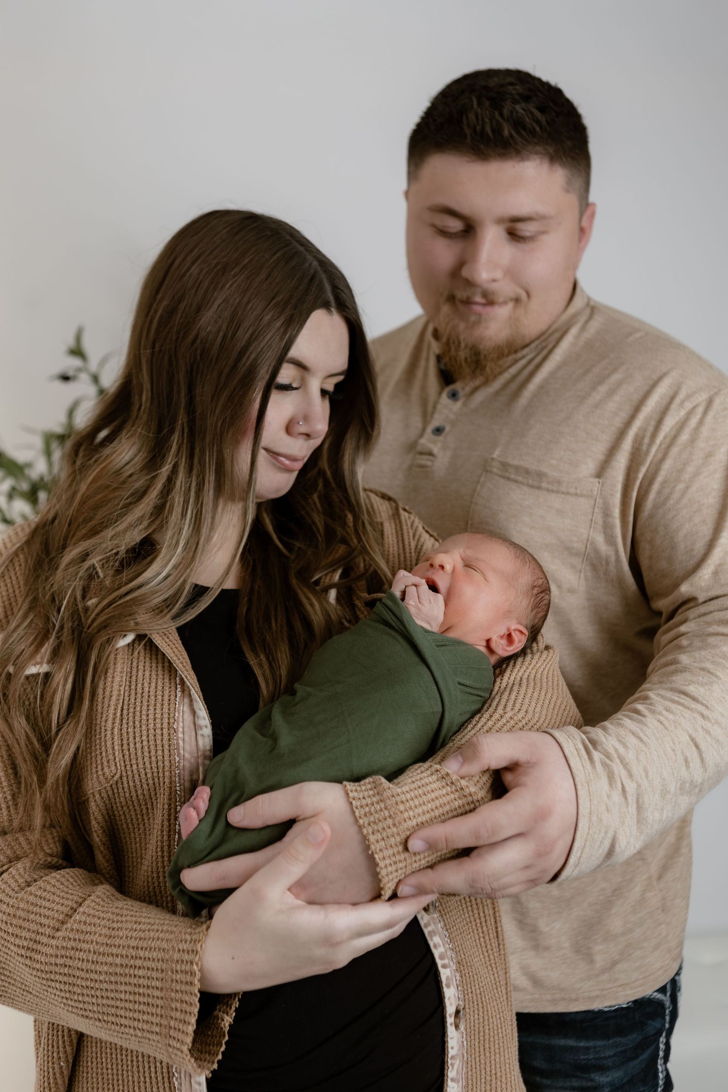 New parents lovingly gazing at their newborn baby wrapped in a green swaddle blanket.