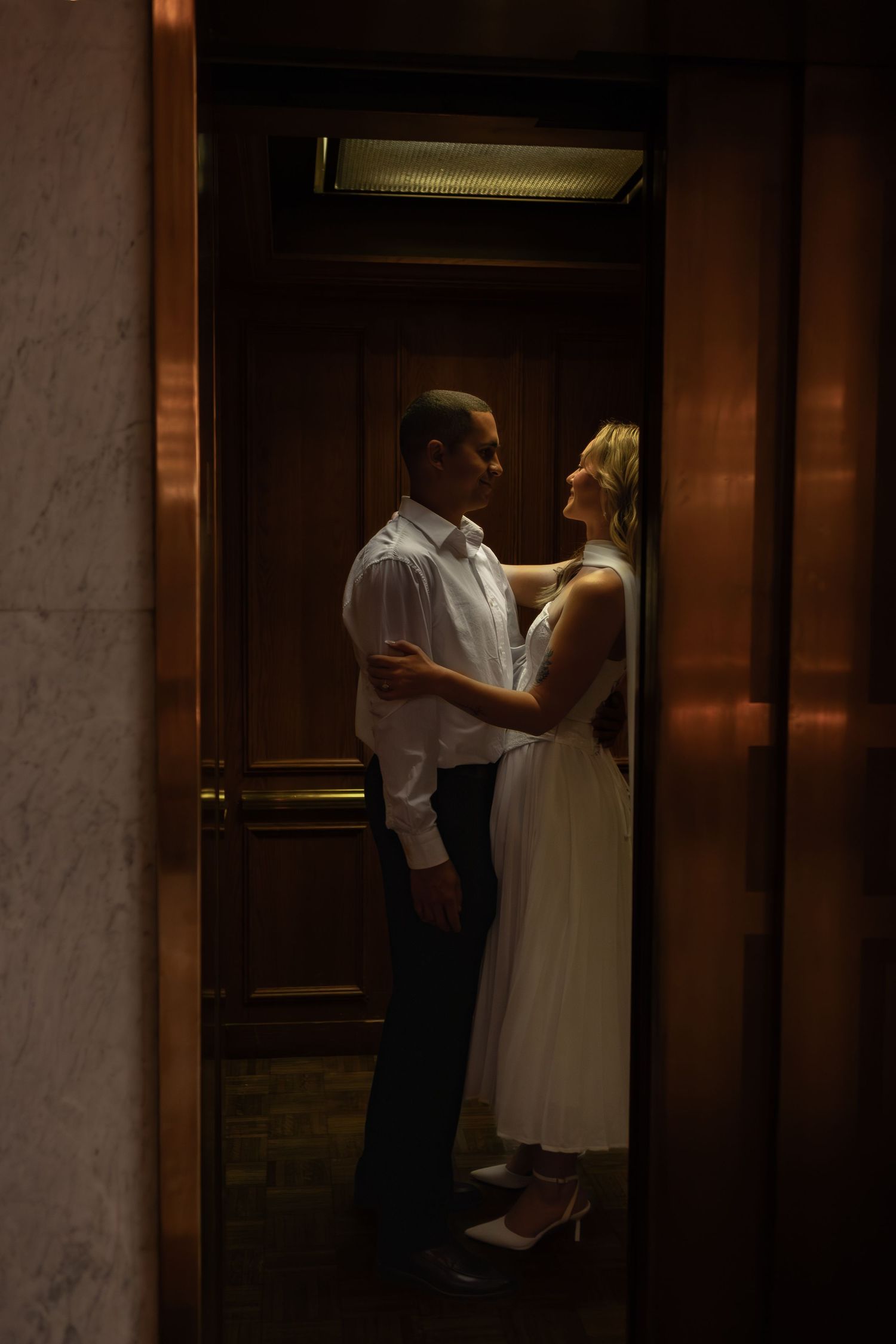 Romantic couple embracing and gazing at each other inside a vintage elevator.