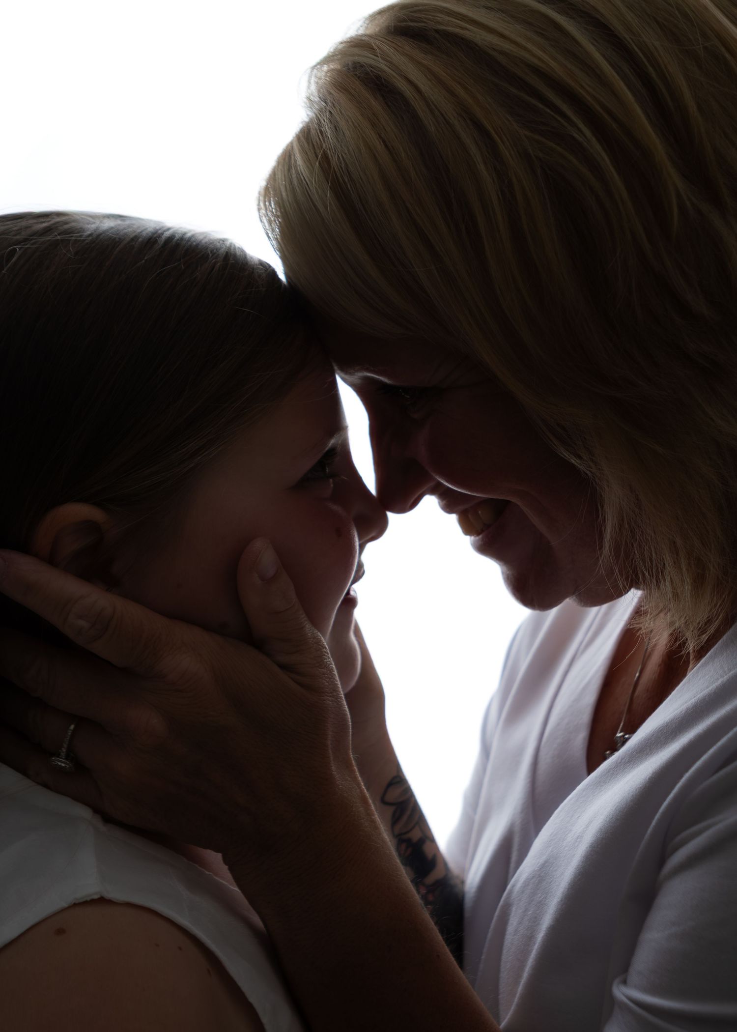 Silhouette of mother and daughter touching foreheads in an intimate backlit portrait.