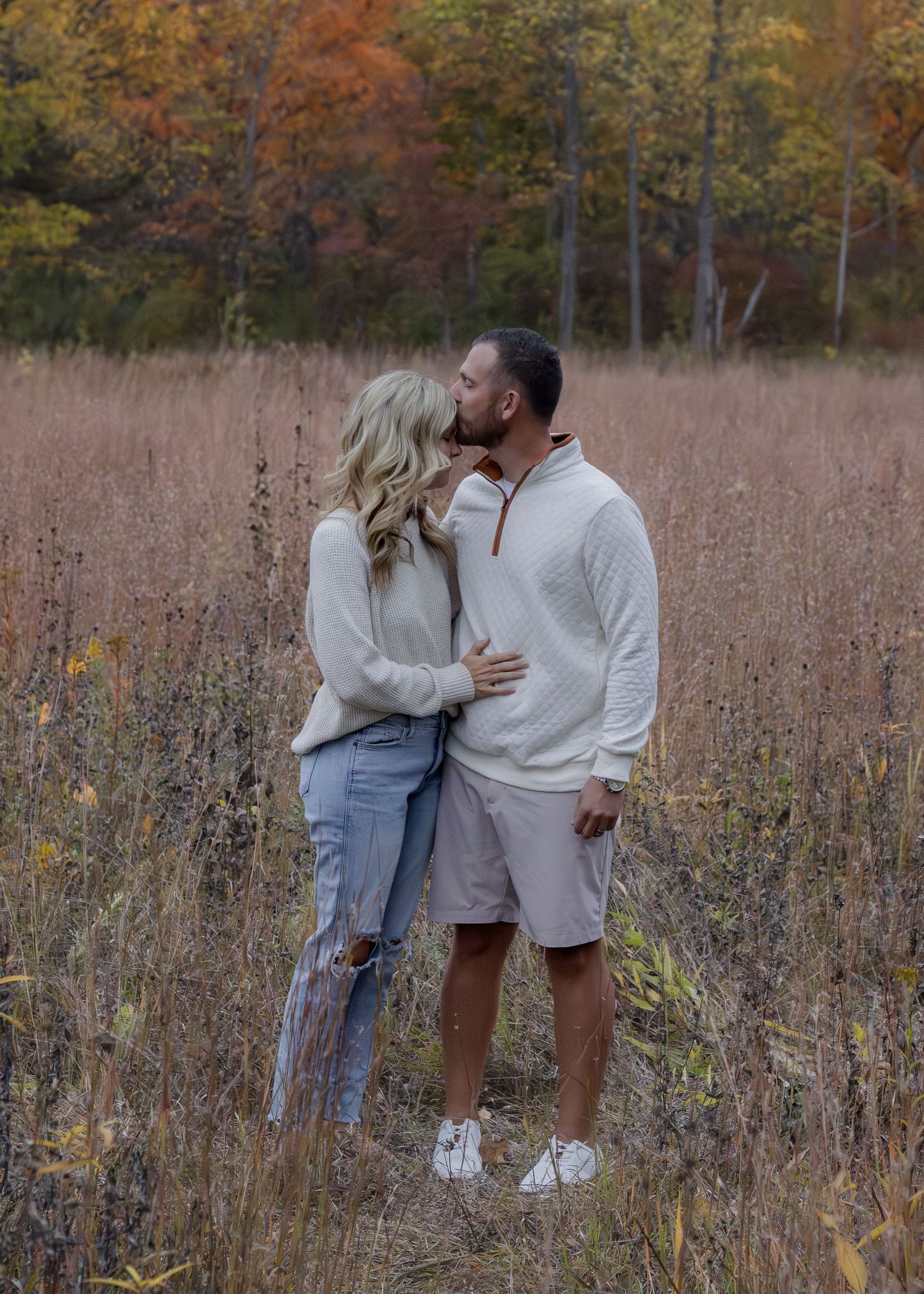 Couple sharing a romantic kiss in an autumn field surrounded by colorful fall foliage.