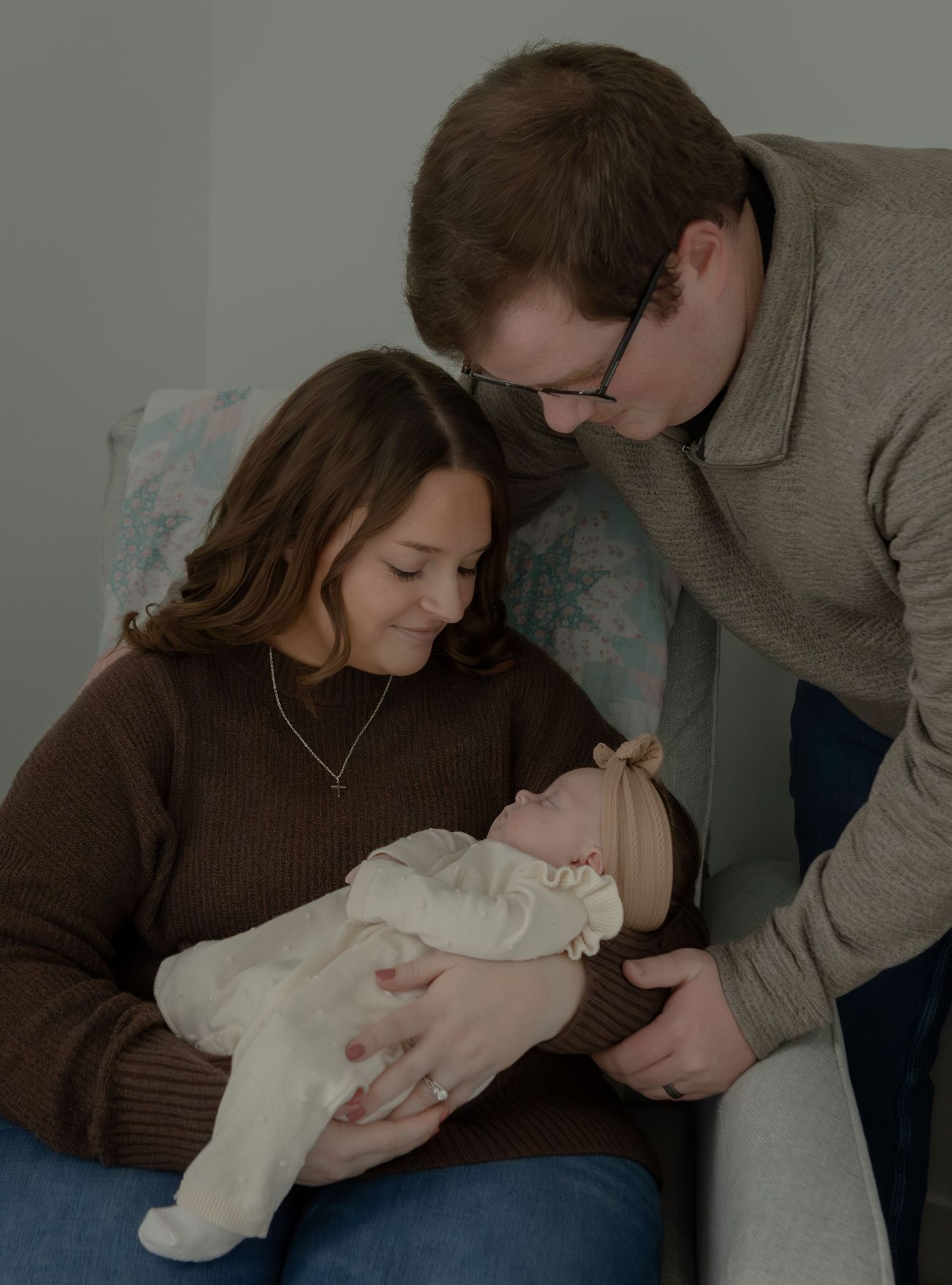 New parents tenderly gazing at sleeping newborn baby during indoor newborn photography session.