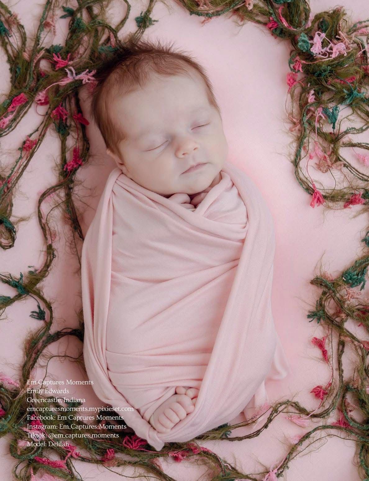 Sleeping newborn baby wrapped snugly in pink swaddle, surrounded by green floral vines on pink background.