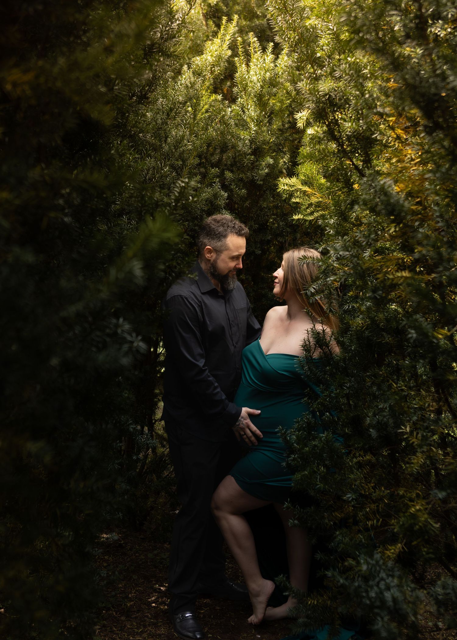 Couple sharing a romantic moment surrounded by lush green bushes in an outdoor garden setting.