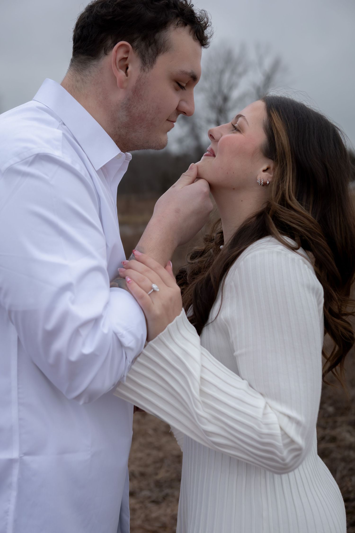 Romantic couple in white outfits sharing an intimate moment outdoors during an engagement photo session.
