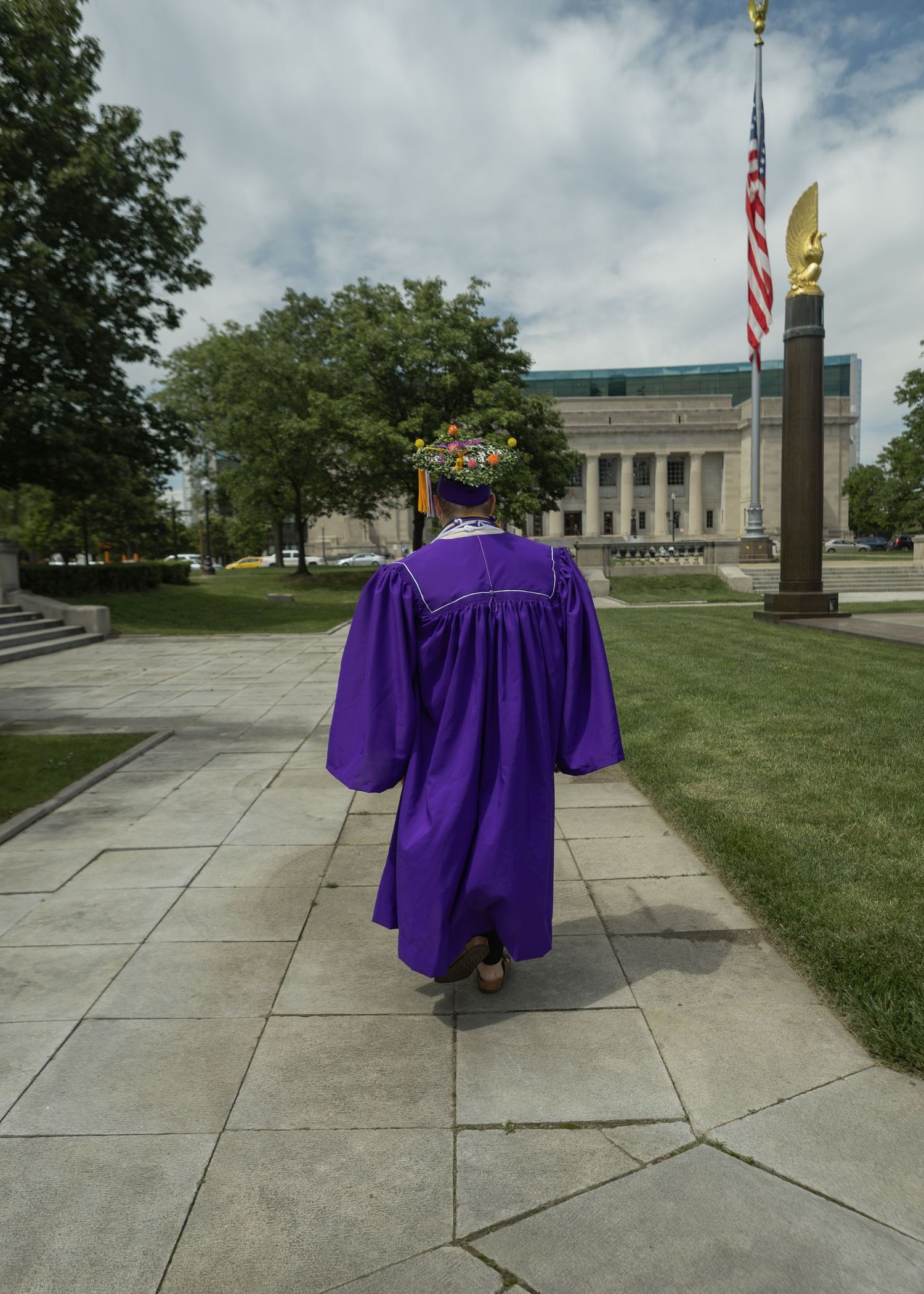 Graduate in purple cap and gown walking along a pathway on a college campus.