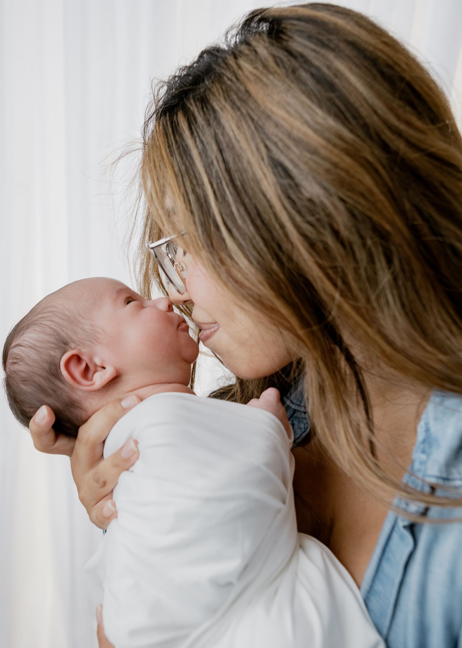 Brunette mother with glasses shares a tender nose-to-nose moment with her newborn baby.