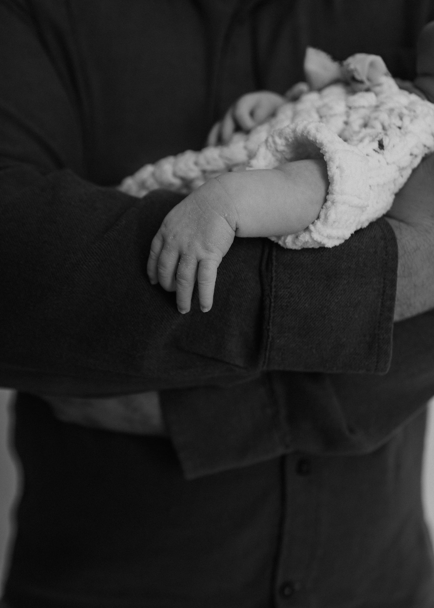 Black and white close-up of a newborn baby being cradled in an adult's arms.