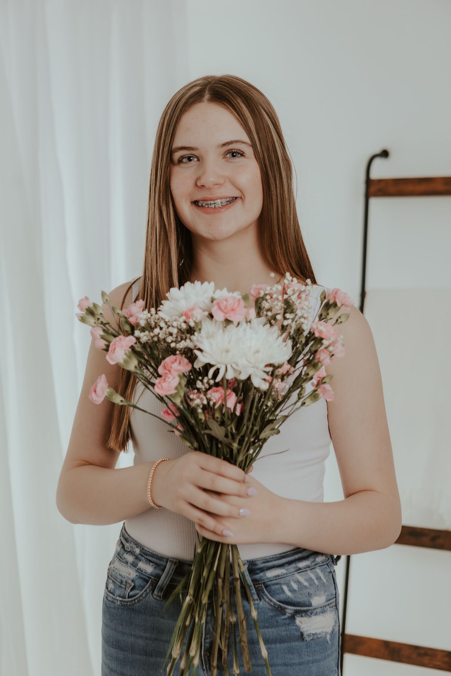 Smiling teenage girl with braces holding bouquet of pink and white flowers indoors.