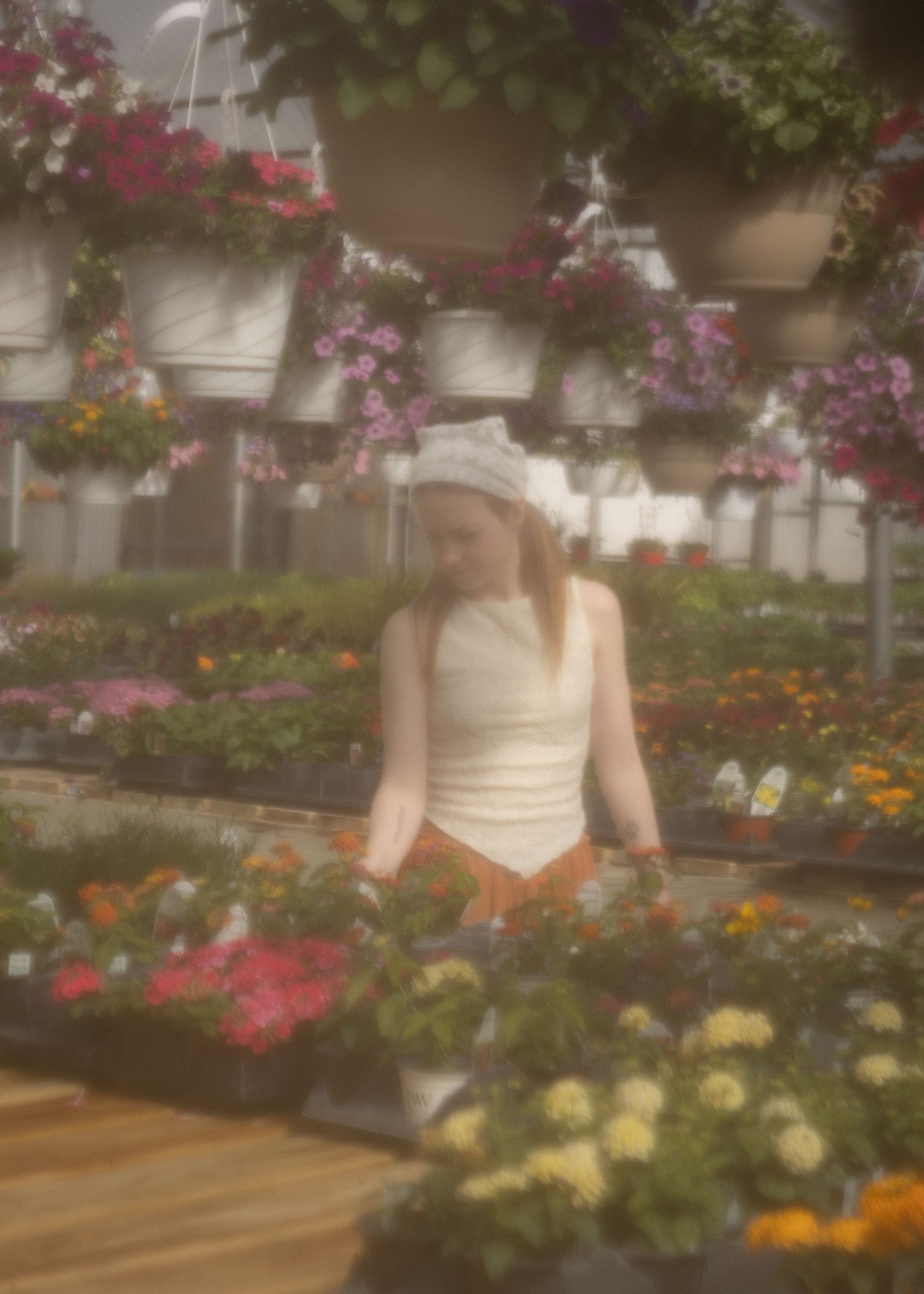 Young woman in white top browsing colorful flowers in a lush greenhouse nursery.
