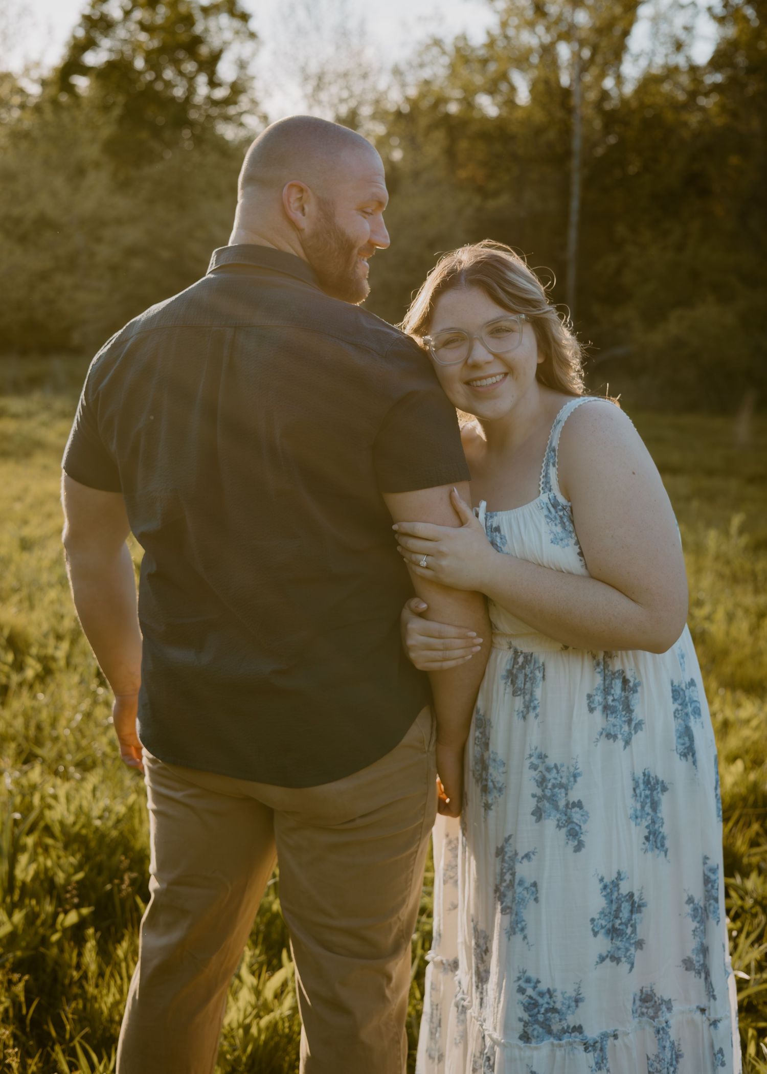 Couple sharing a tender moment at golden hour in a sunlit meadow, woman smiling in floral dress.