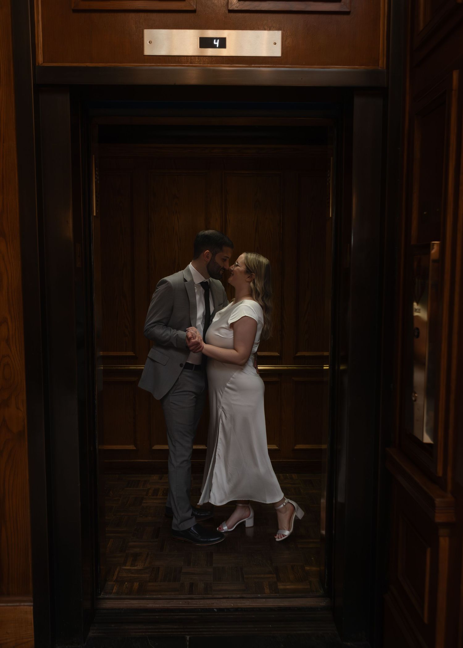 Couple sharing a romantic kiss inside a vintage wooden elevator with warm ambient lighting.