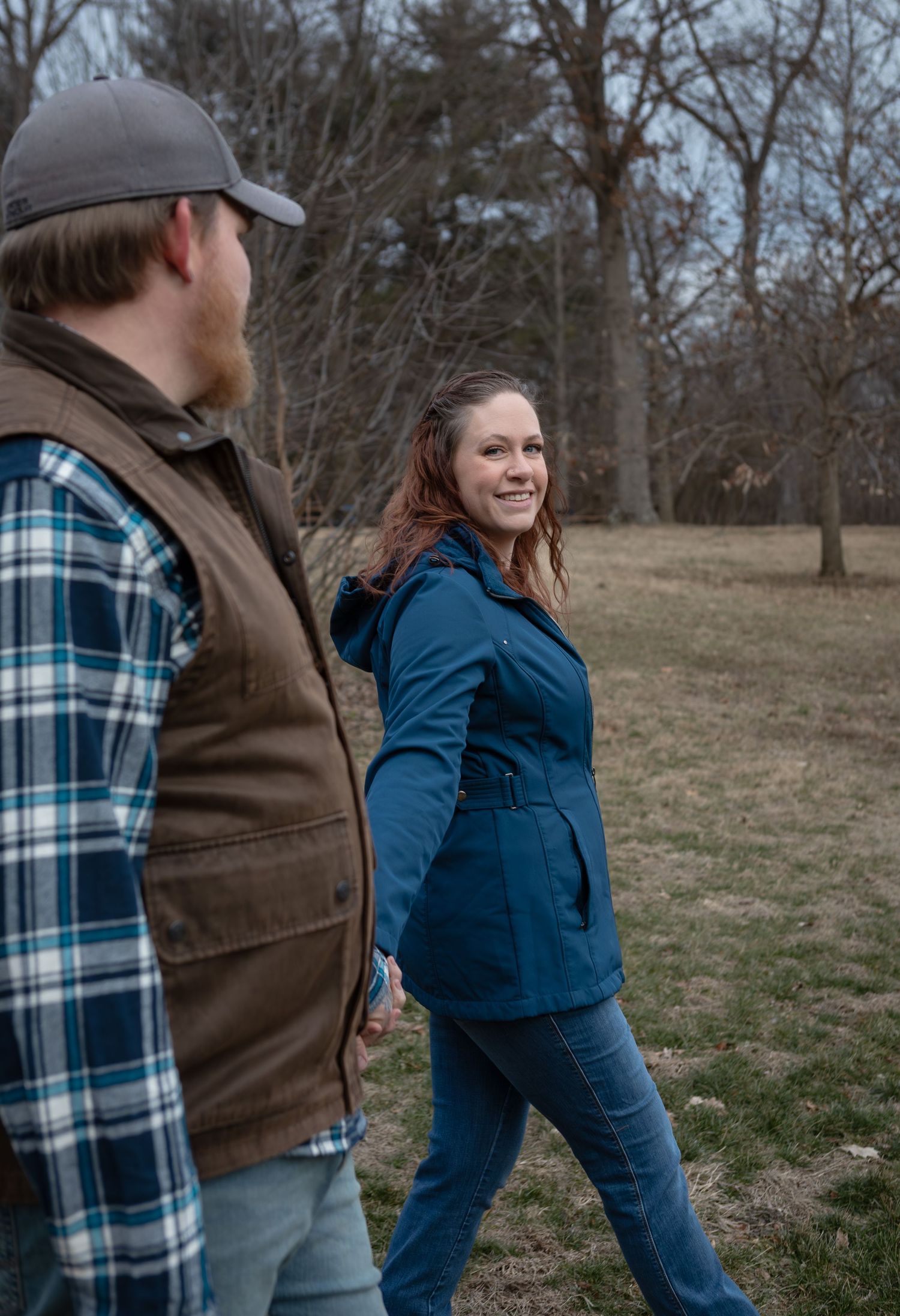Couple walking outdoors in a park, woman in blue jacket smiling back at her partner.