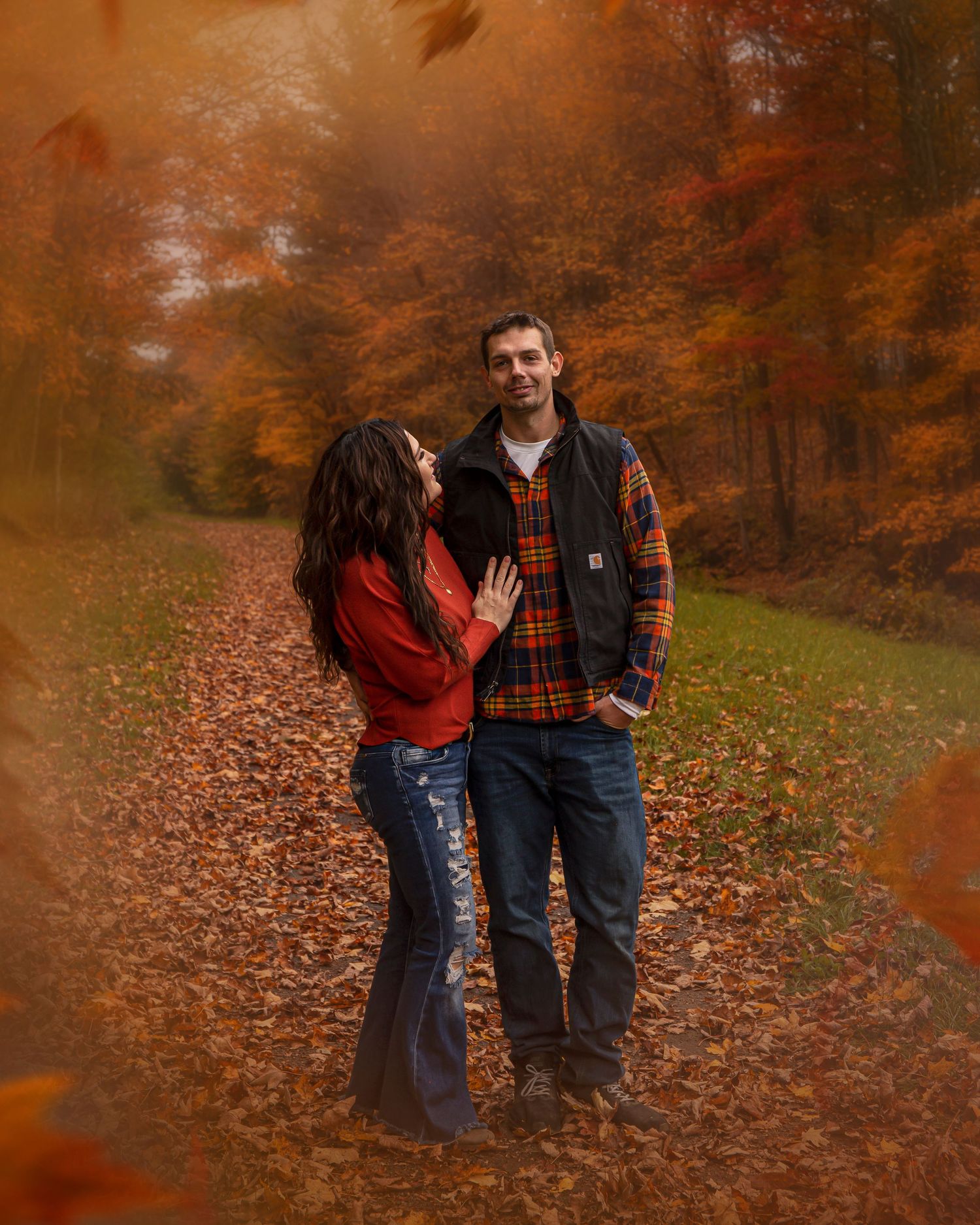 Couple walking through fallen autumn leaves on a path surrounded by orange foliage.