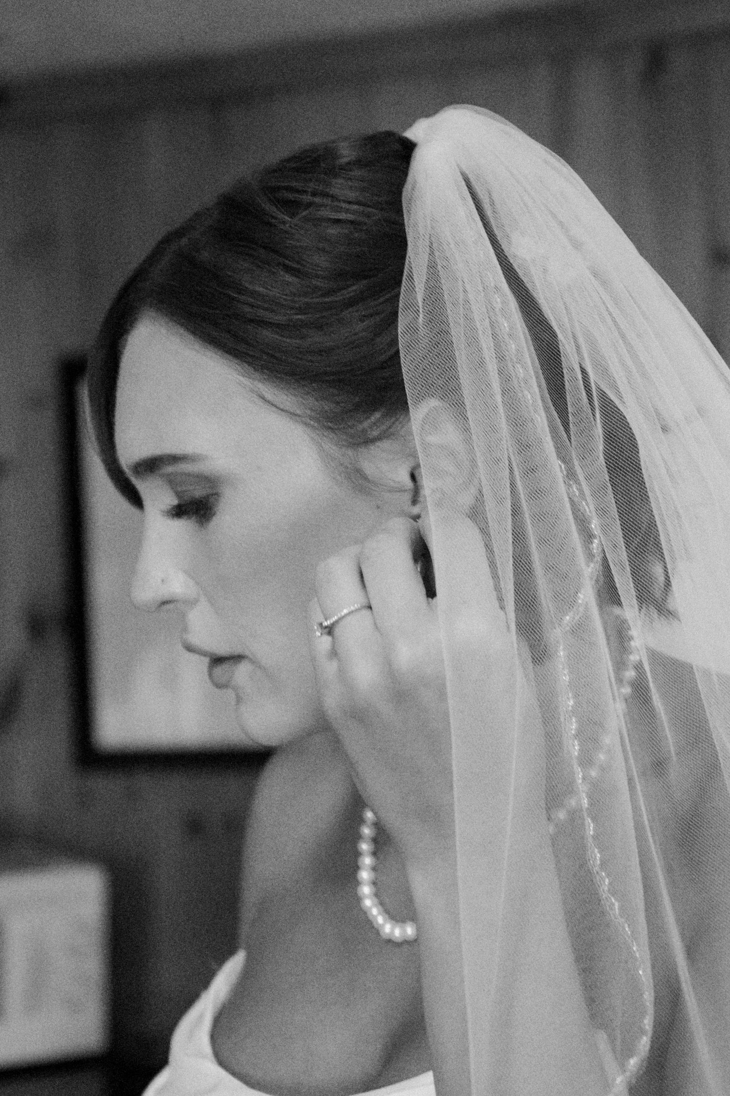 A bride in black and white wearing pearls and a sheer wedding veil shown in elegant profile view.