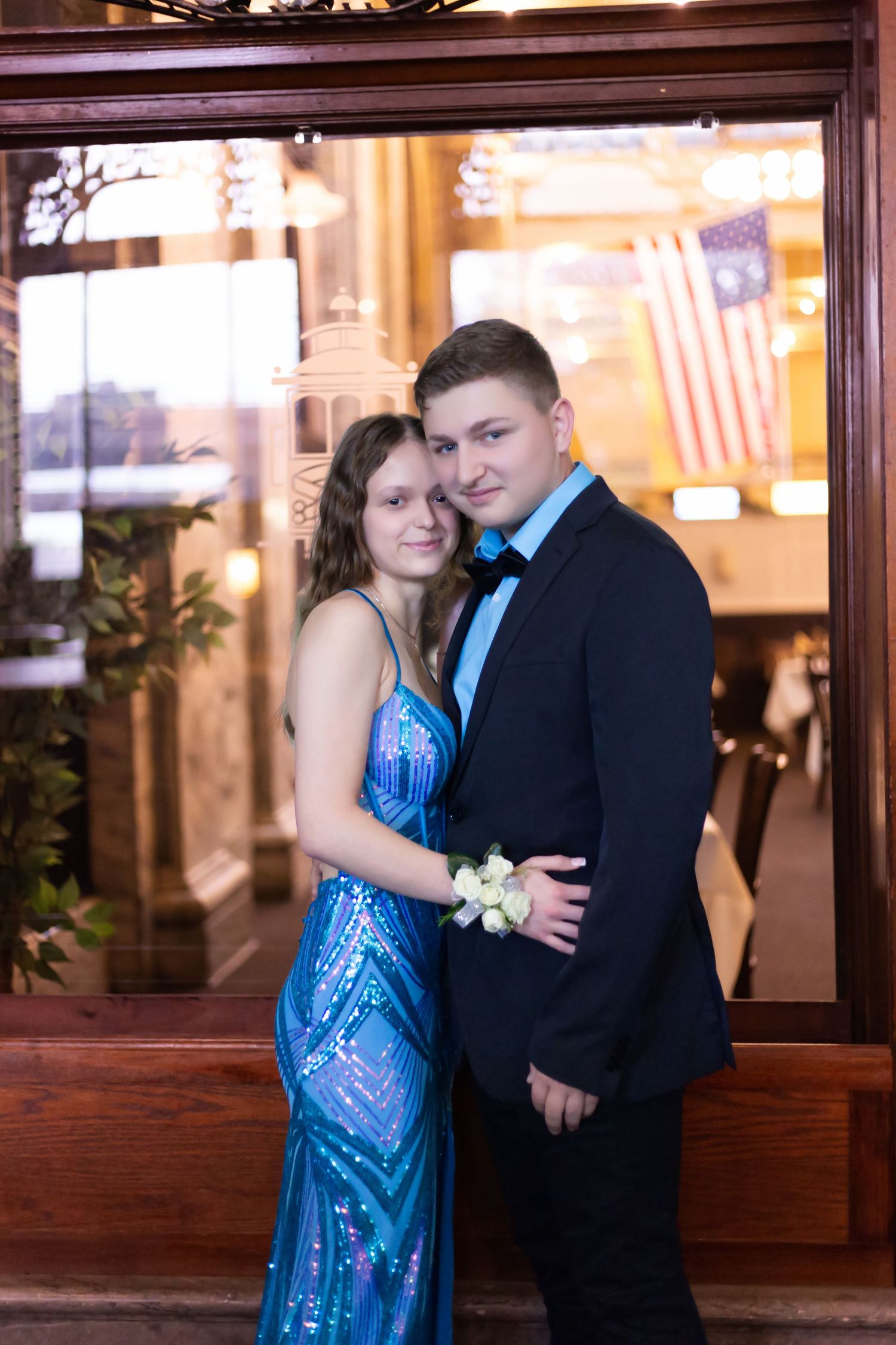 Formal couple in blue dress and suit posing together at an indoor venue with wooden paneling.
