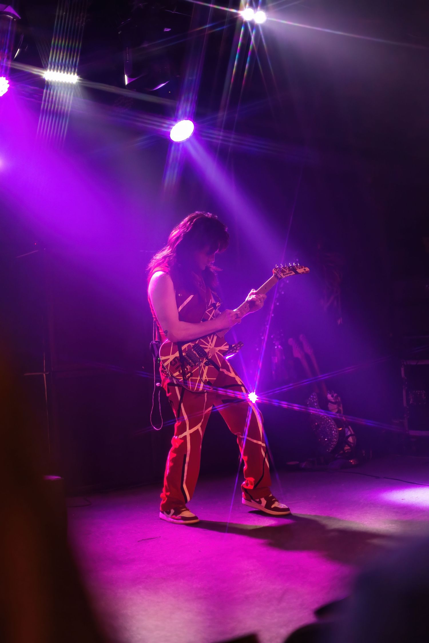A guitarist performs on stage under vibrant purple spotlights during a live rock concert.
