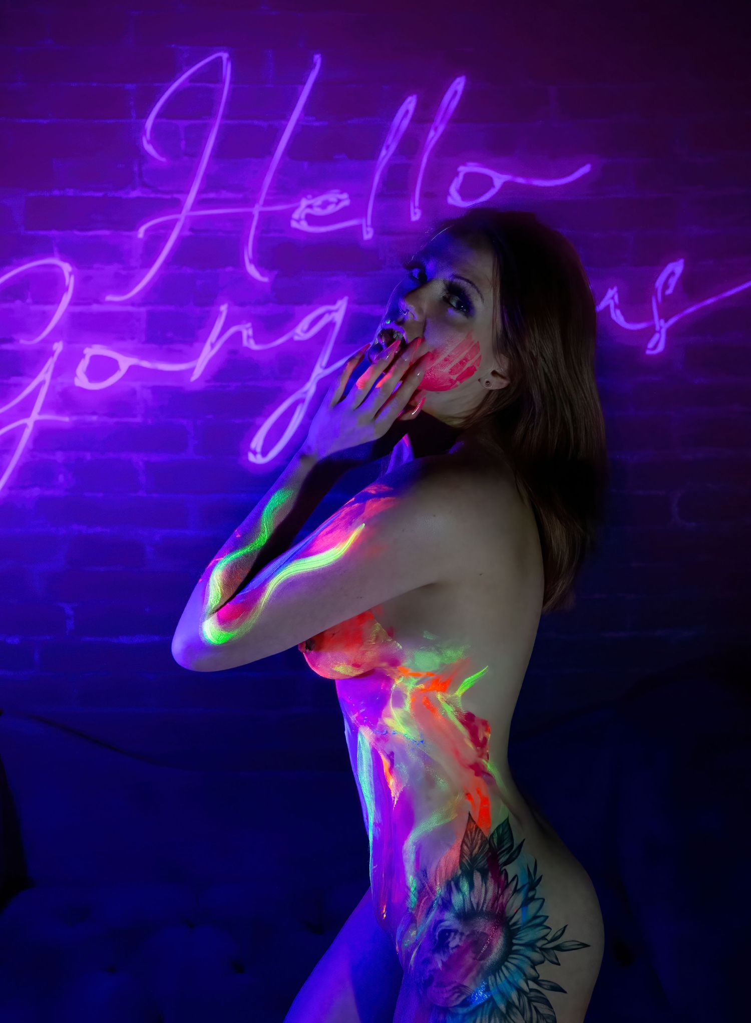Artistic portrait with neon purple lighting and body paint glowing against dark background, featuring 