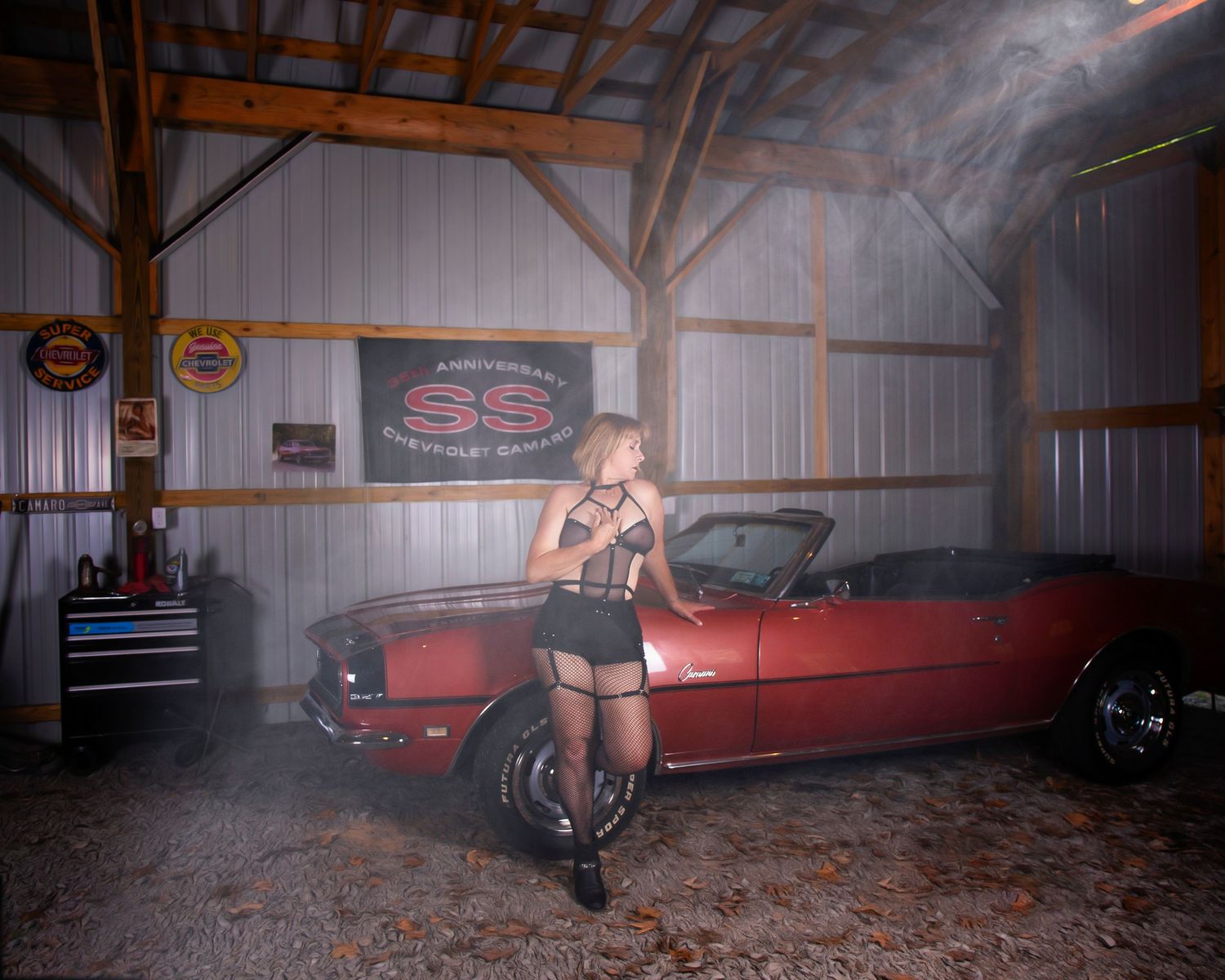 A panoramic view of a dimly lit barn interior with vintage cars parked inside and atmospheric smoke effects.