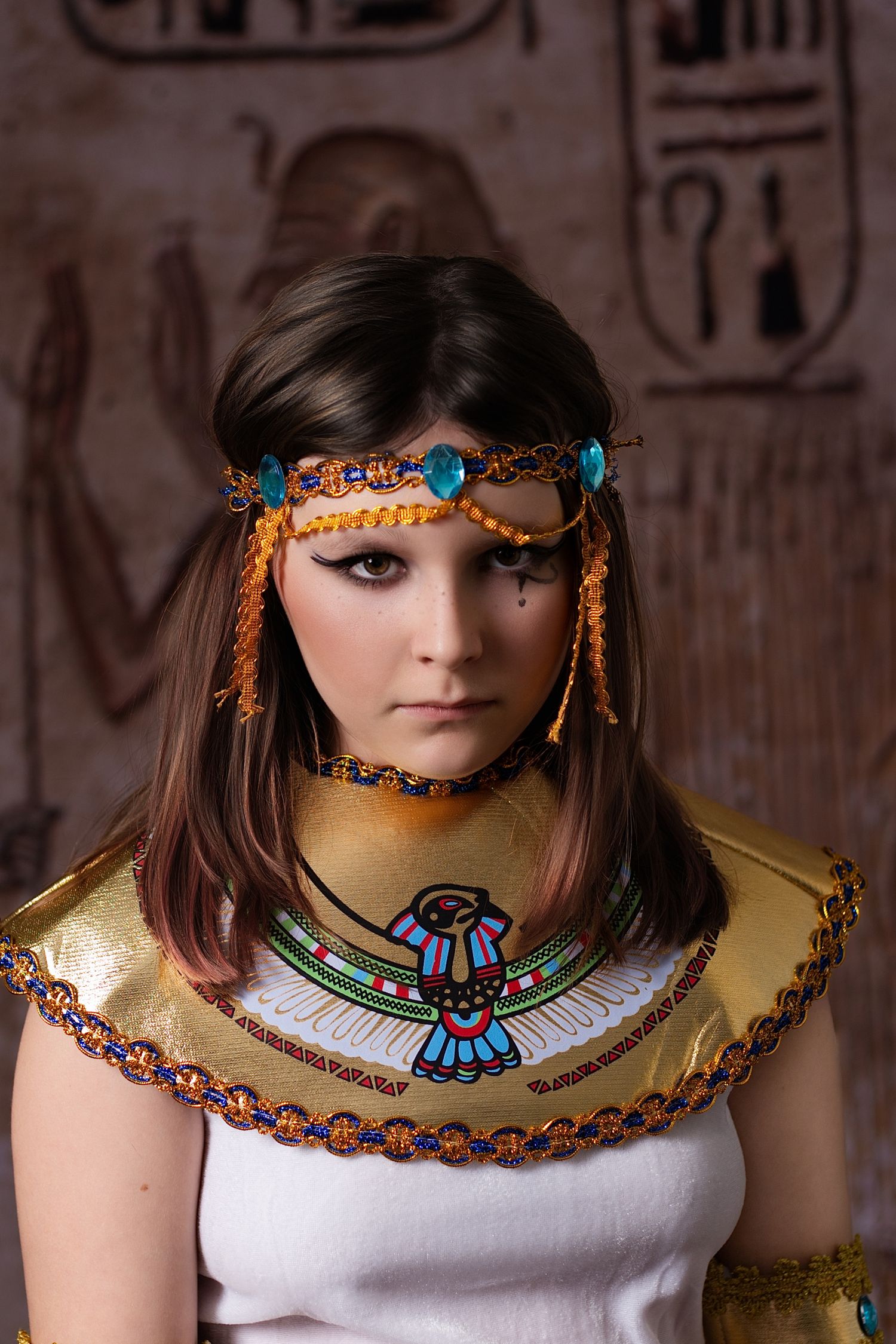 Egyptian-inspired photoshoot with beaded collar necklace and turquoise accessories against hieroglyph wall background.