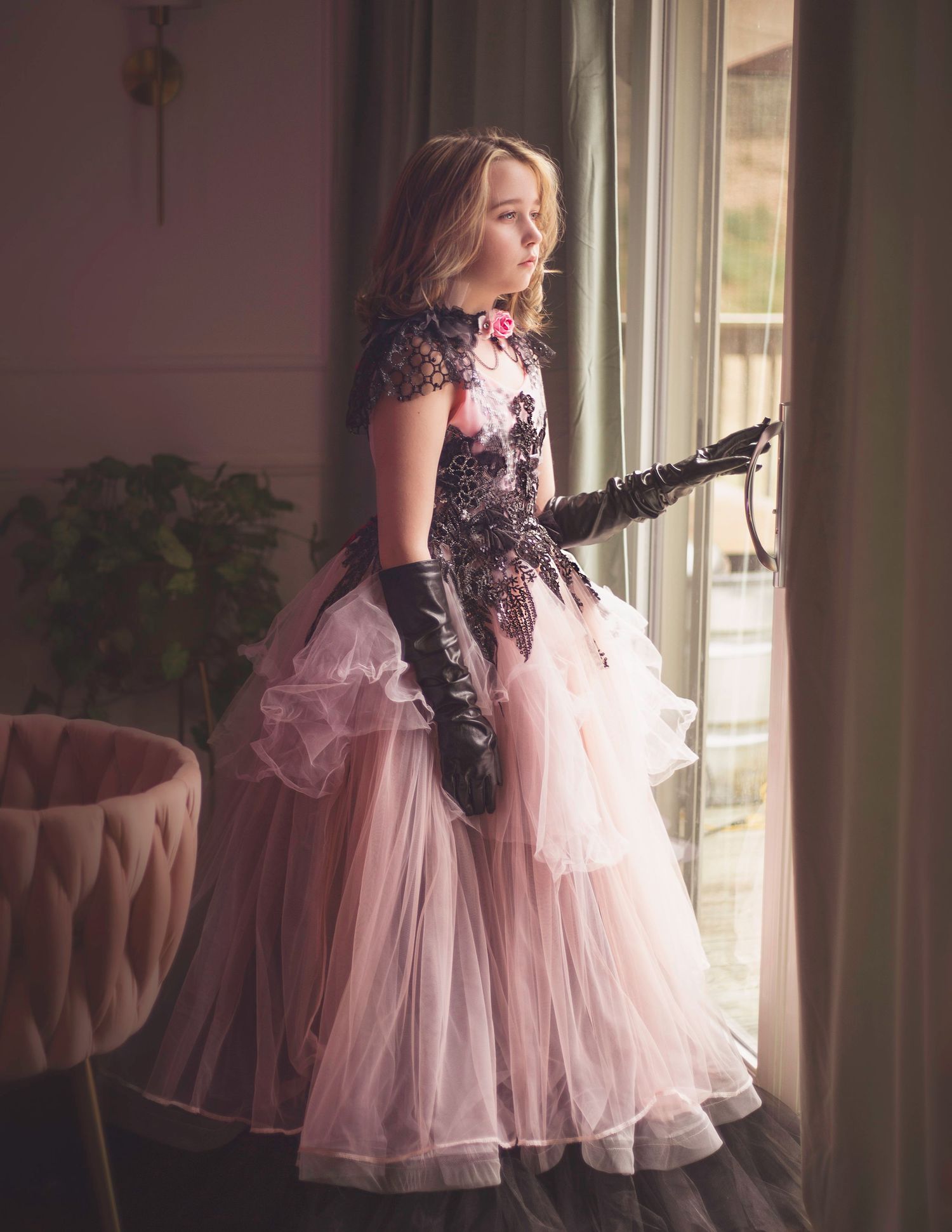 A child in a pink tulle dress twirls in front of a sunlit window in an elegant room.