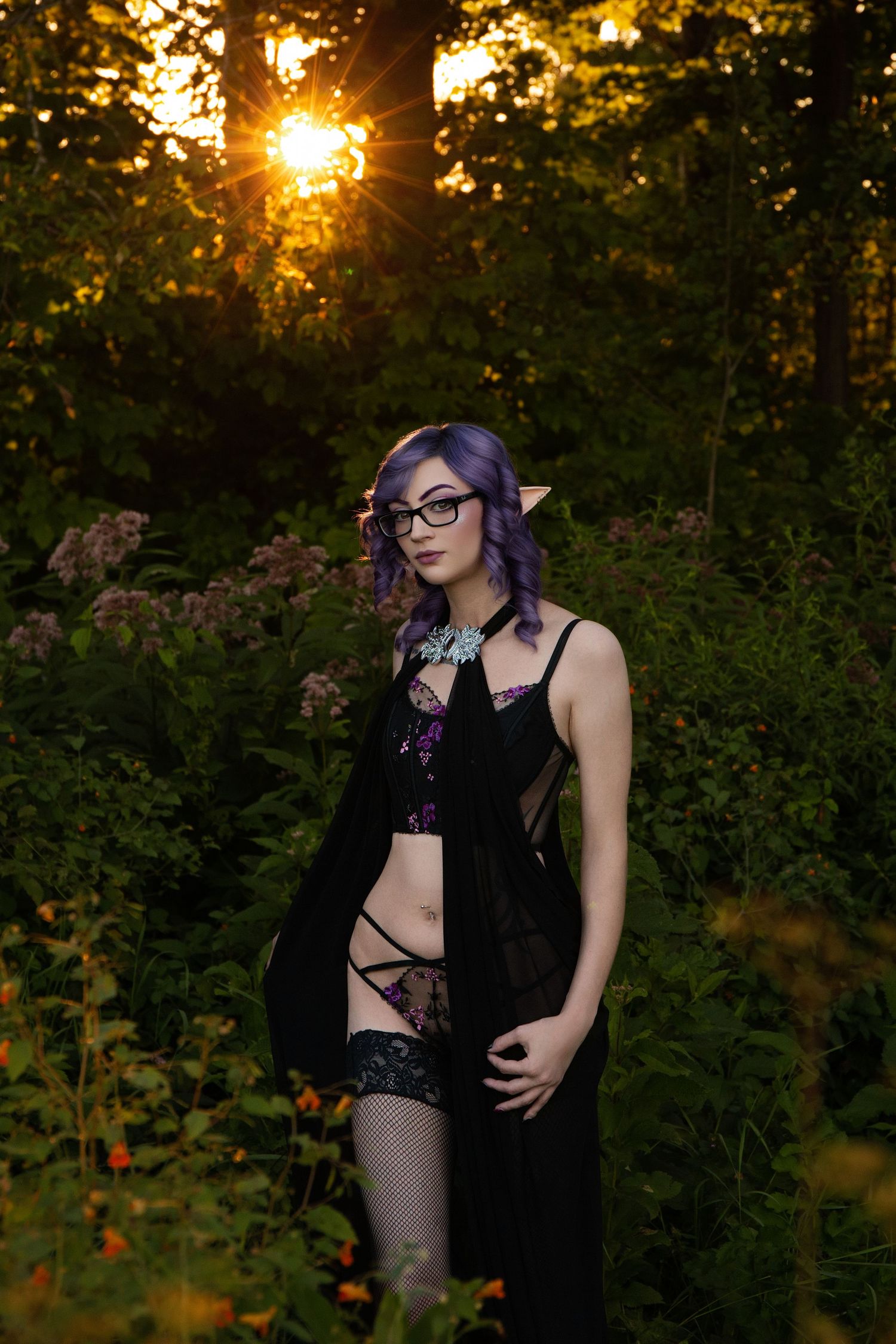 Outdoor photoshoot at sunset with purple hair and black attire in natural foliage.