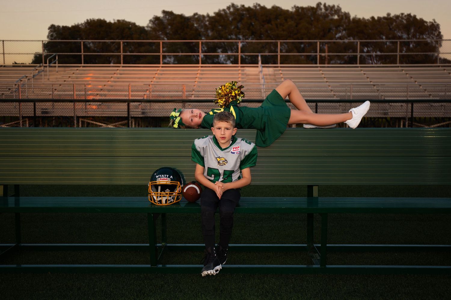 Football player in green uniform lying dramatically across stadium bleachers.