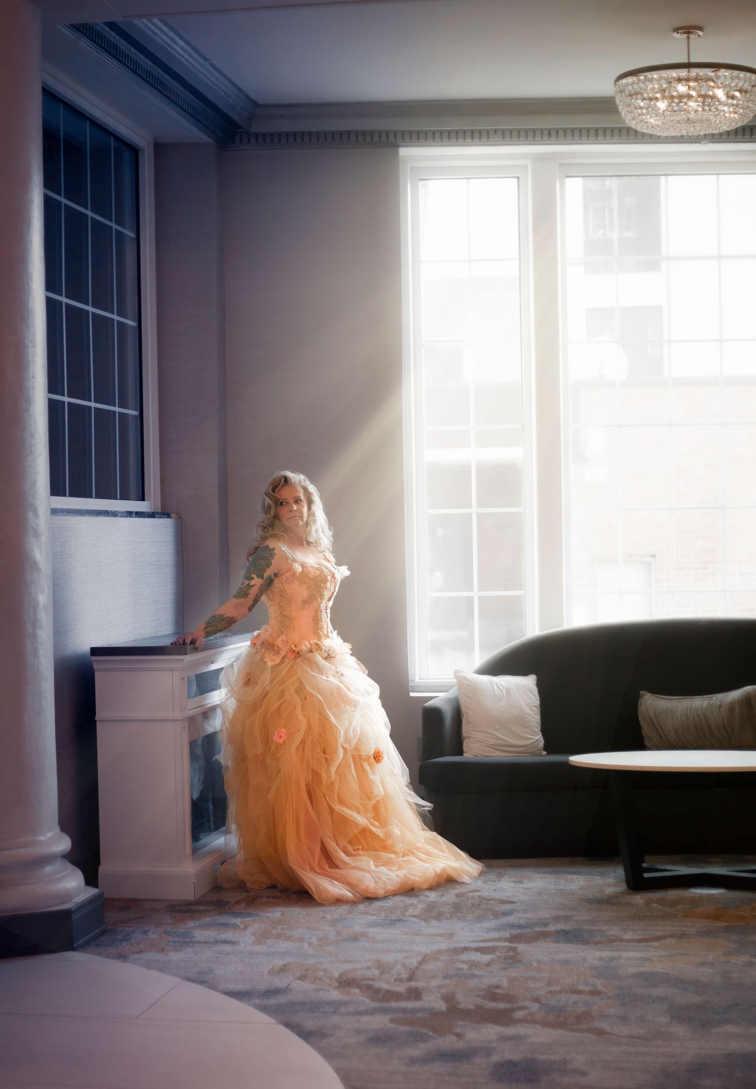 A person in a peach-colored ballgown poses in a sunlit room with modern furnishings.