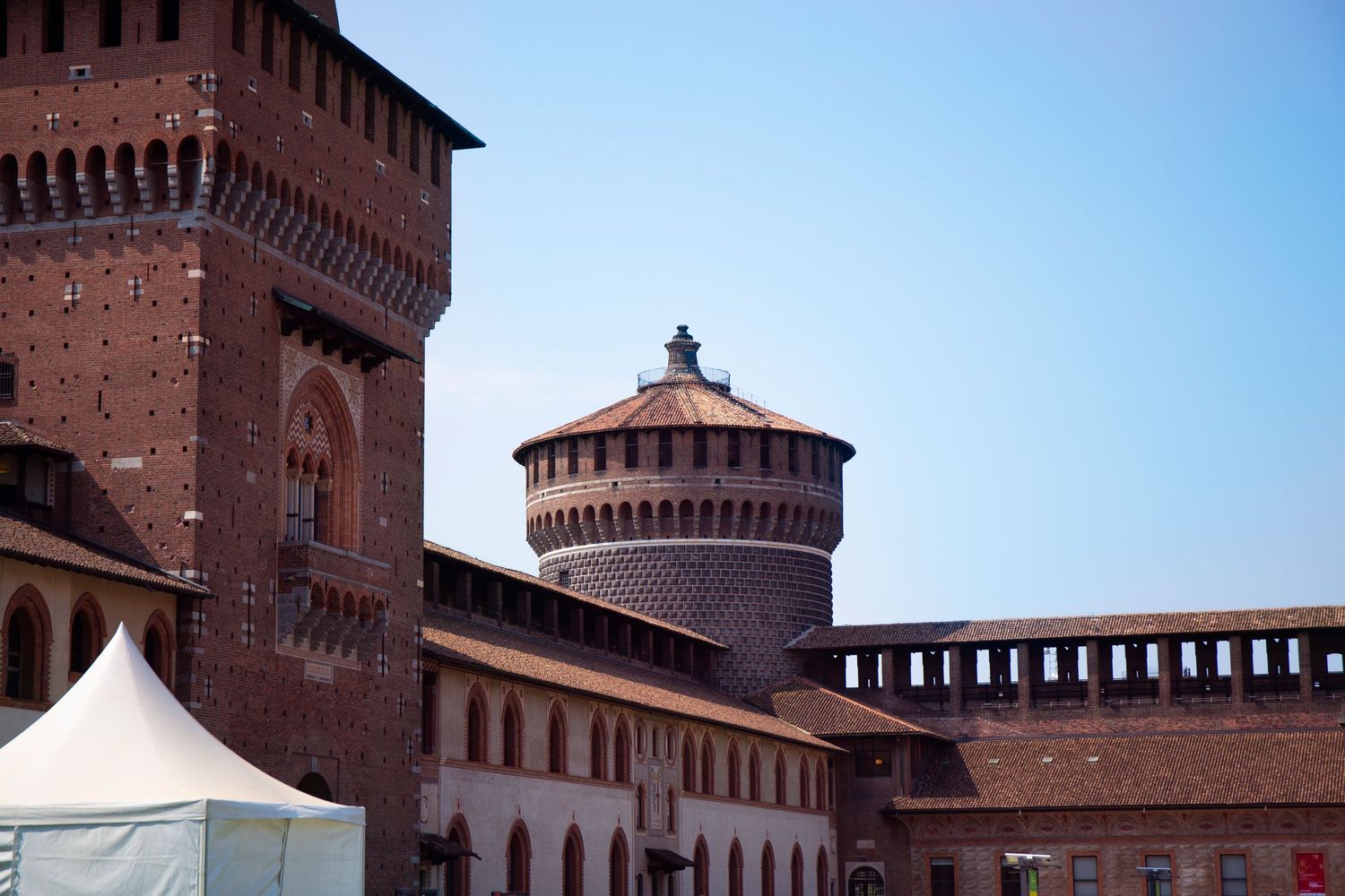 Medieval brick fortress Castello Sforzesco in Milan features ornate towers and crenellated walls against blue sky.