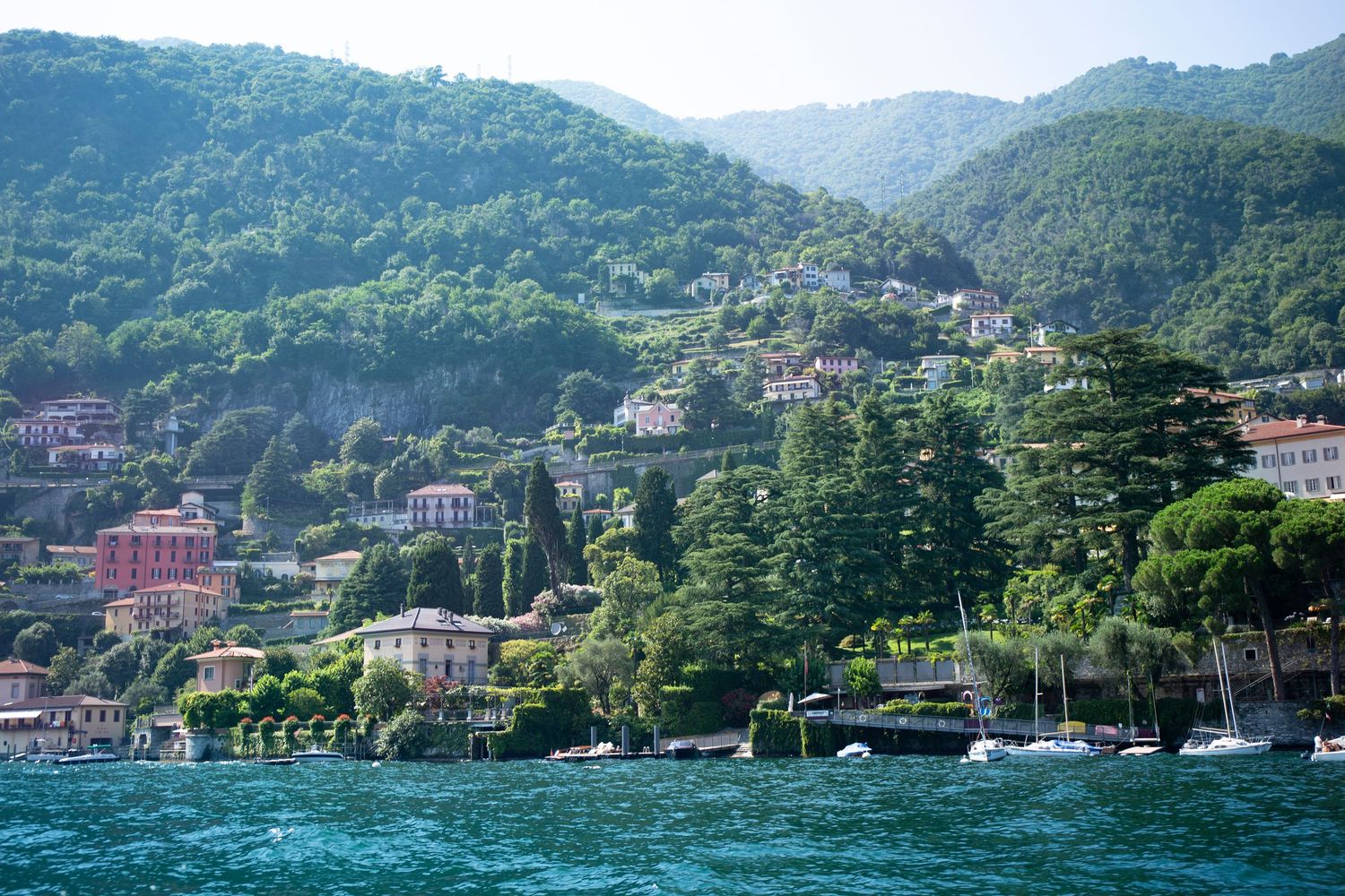 Scenic panoramic view of Lake Como's shoreline with luxury villas nestled among lush green mountains in Italy.
