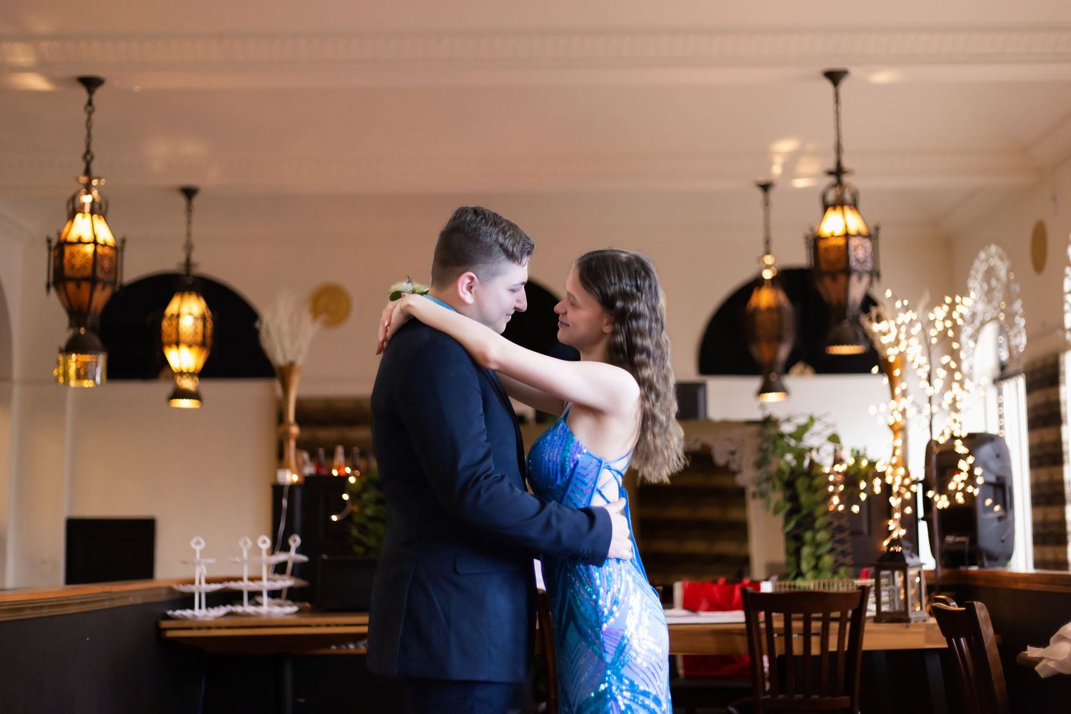A couple embraces during an intimate dance in an elegant venue decorated with hanging lanterns and twinkle lights.