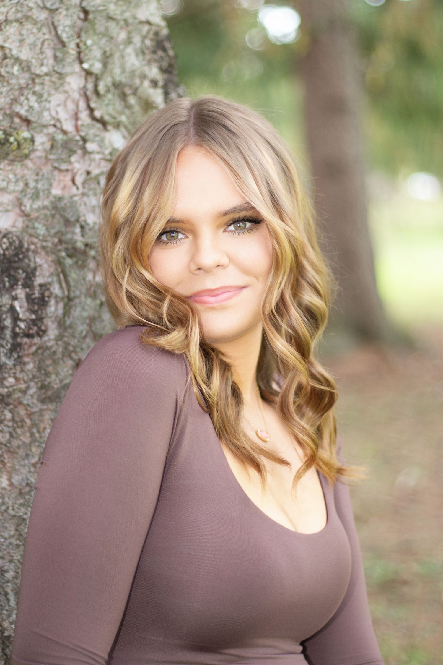 Portrait of person in brown top against tree bark background with soft natural lighting.