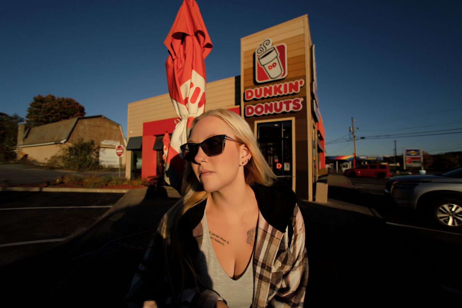 Red-haired person in sunglasses poses against a bright blue sky with buildings in the background.