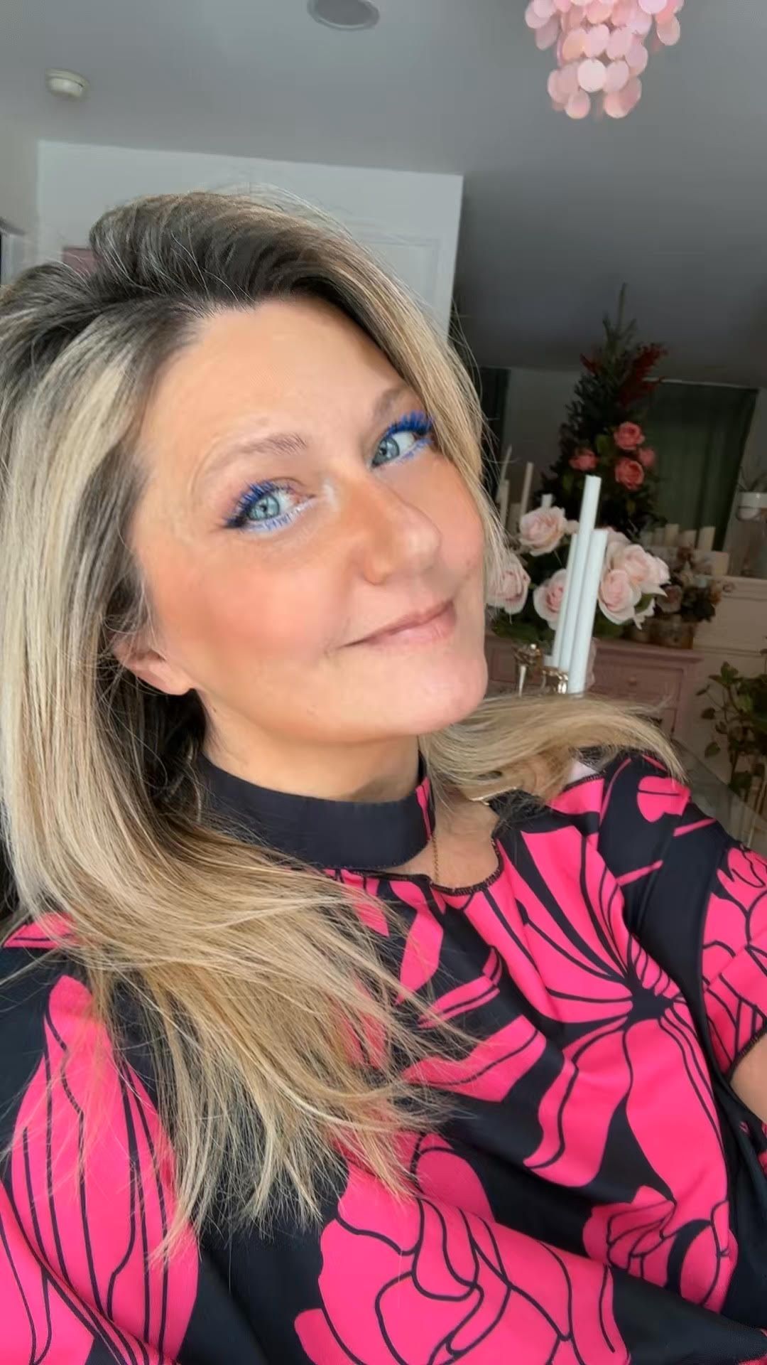 A selfie showing blonde hair and bright blue eyes wearing a black and hot pink floral print top.
