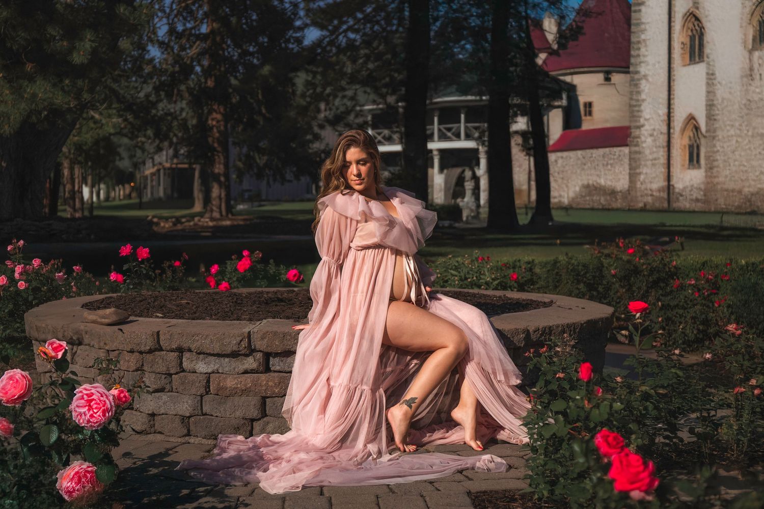 Romantic portrait session with pink dress against stone wall and red flowers.
