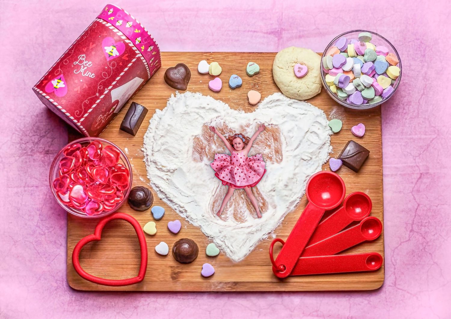 Valentine's day baking setup with heart shapes, sprinkles, and pink decorations on wooden board.