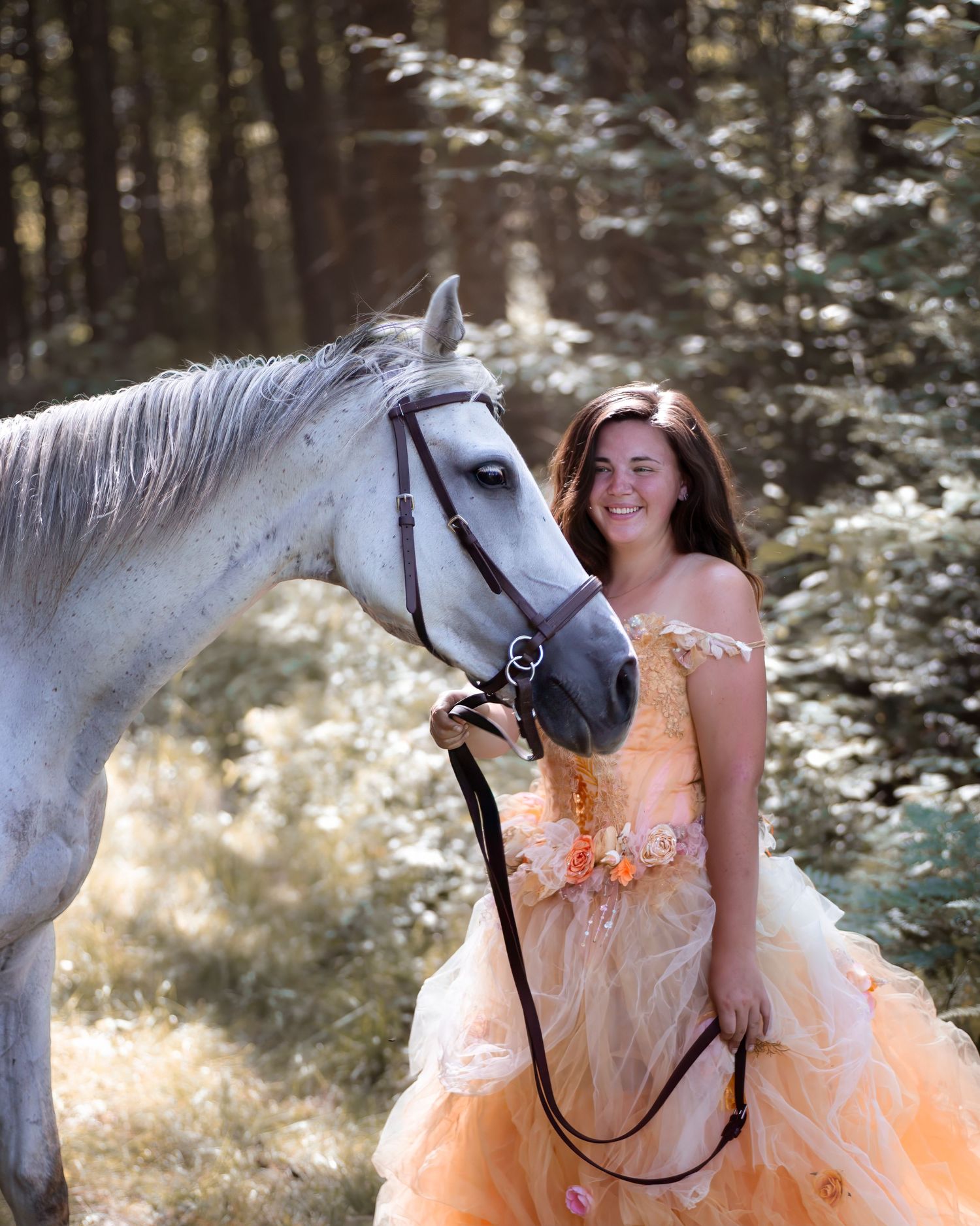 A dreamy portrait with a white horse in a forest setting wearing a peach-colored gown.