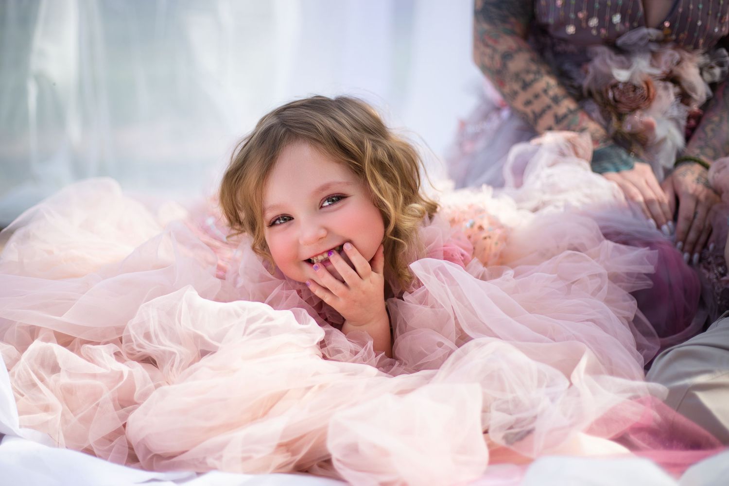 Child in pink tulle dress lying on soft blankets during dreamy portrait session.