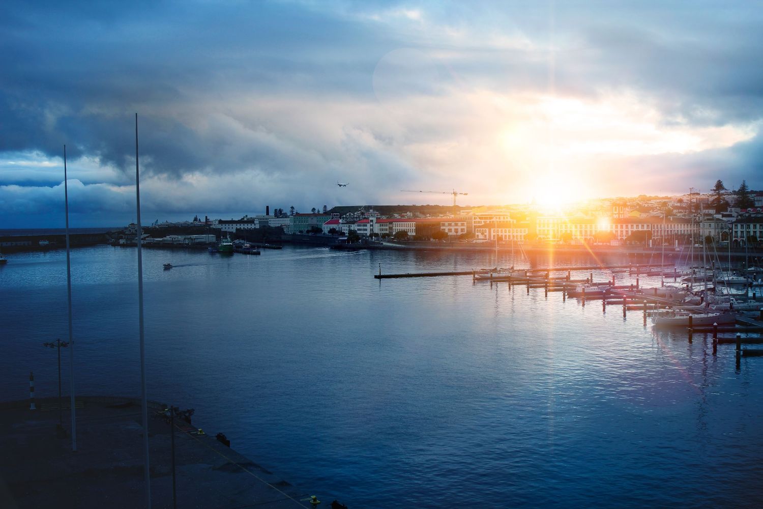 Dramatic sunset illuminates a peaceful marina with boats docked along the waterfront as storm clouds gather overhead.