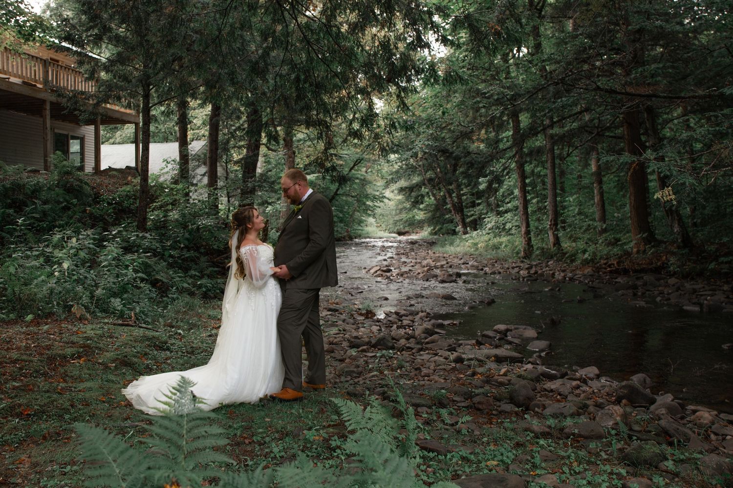 Newlyweds share intimate moment on wooded path during wedding photoshoot.