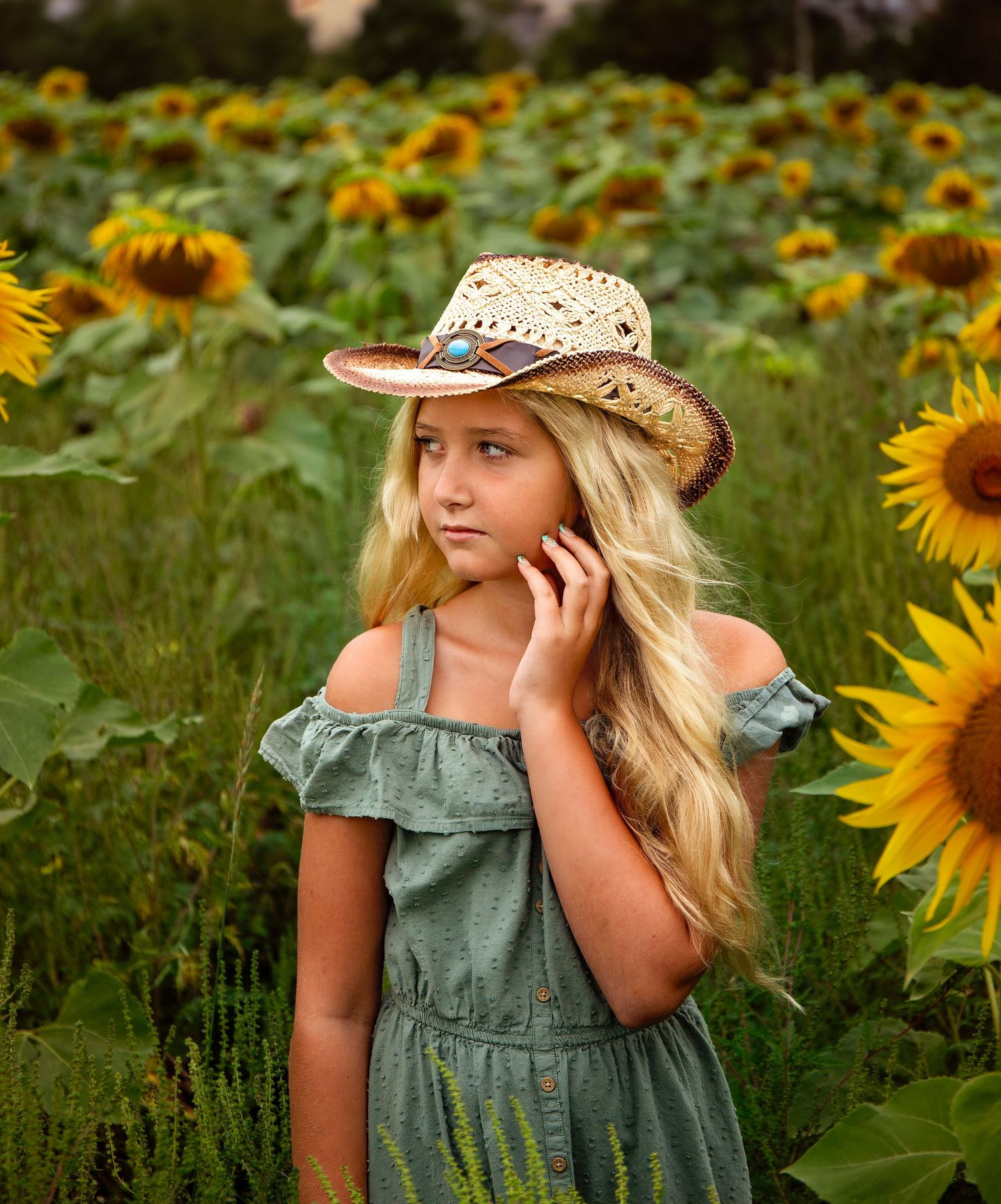 Rustic summer portrait in a sunflower field with vintage straw hat.