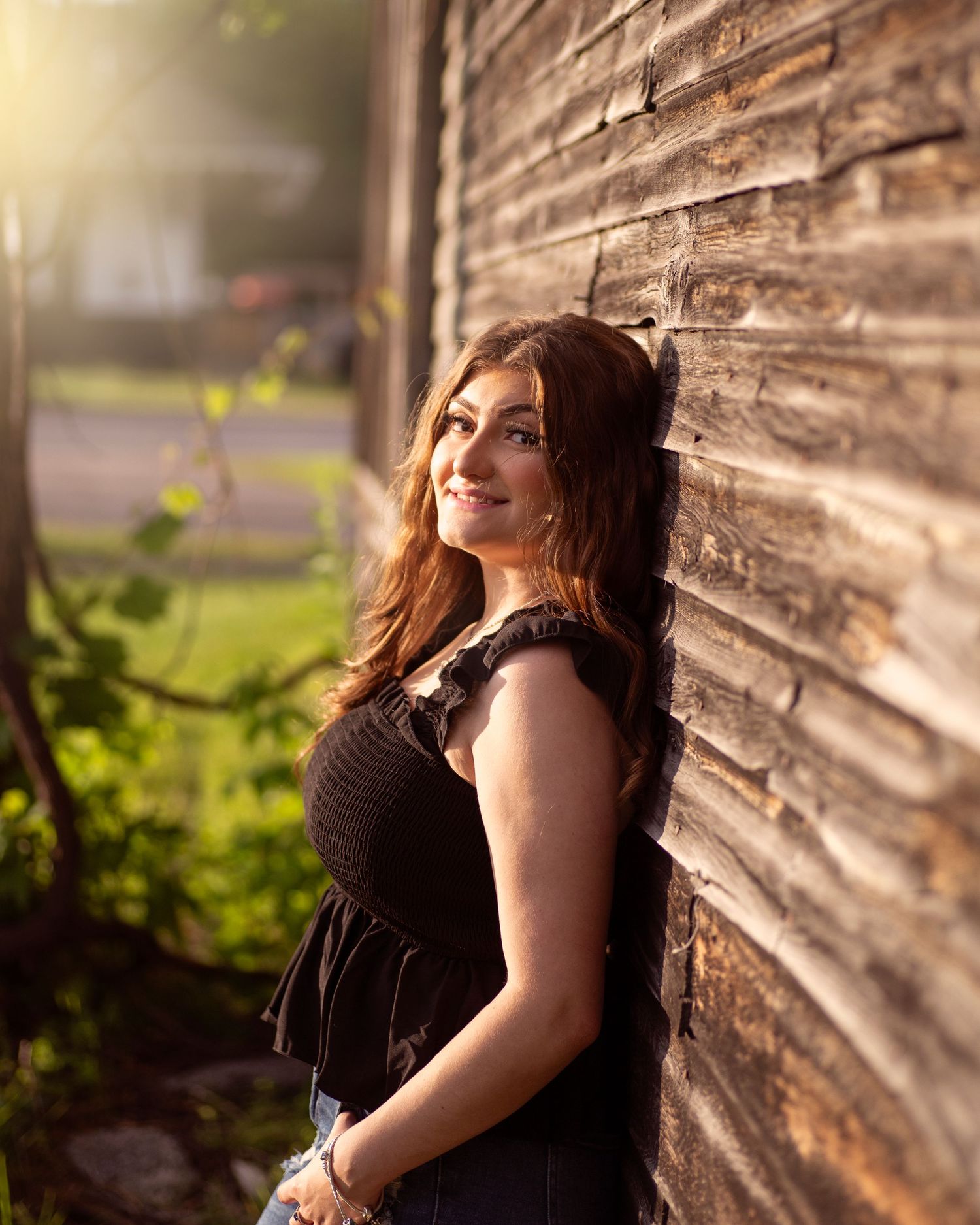 A maternity portrait against a rustic wooden wall in warm natural lighting.
