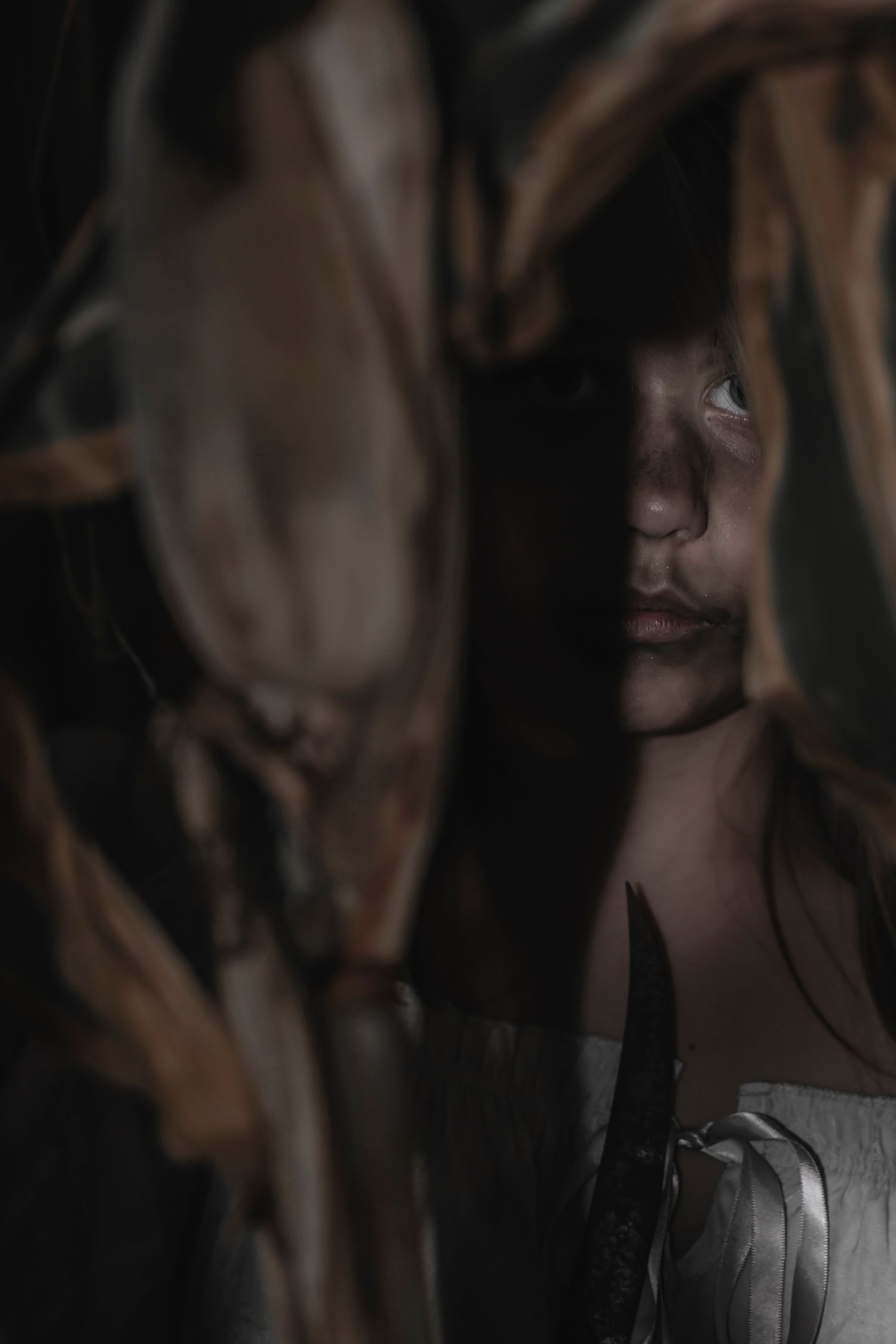 A moody dark portrait with dramatic shadows and soft light illuminating part of a figure through leaves or branches.