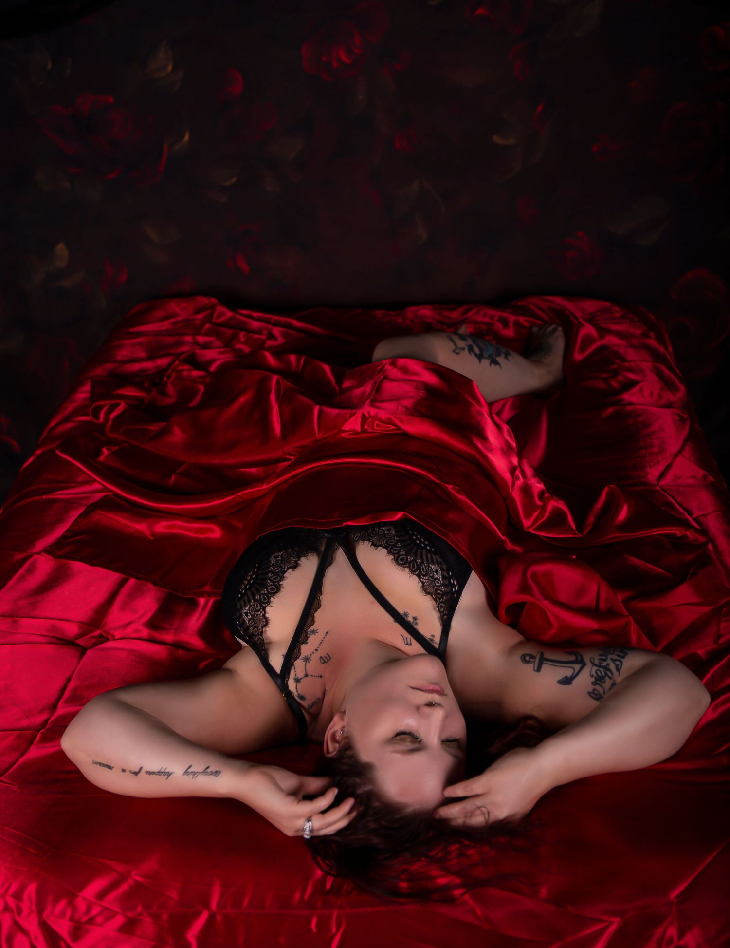 Artistic portrait on red satin sheets with dramatic lighting and black lace details.