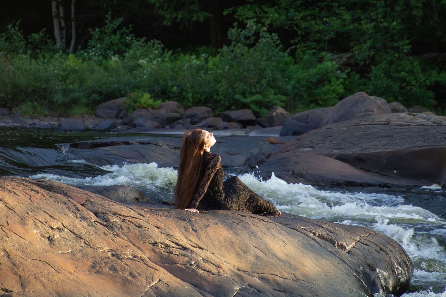 Scenic waterfall flows over rocky ledges in a lush forest setting during golden hour lighting.